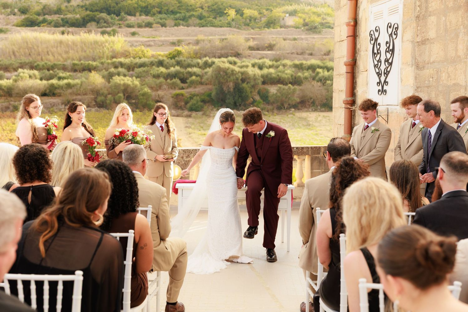 Wedding ceremony guests stand in a row at an outdoor venue with desert landscape in the background.