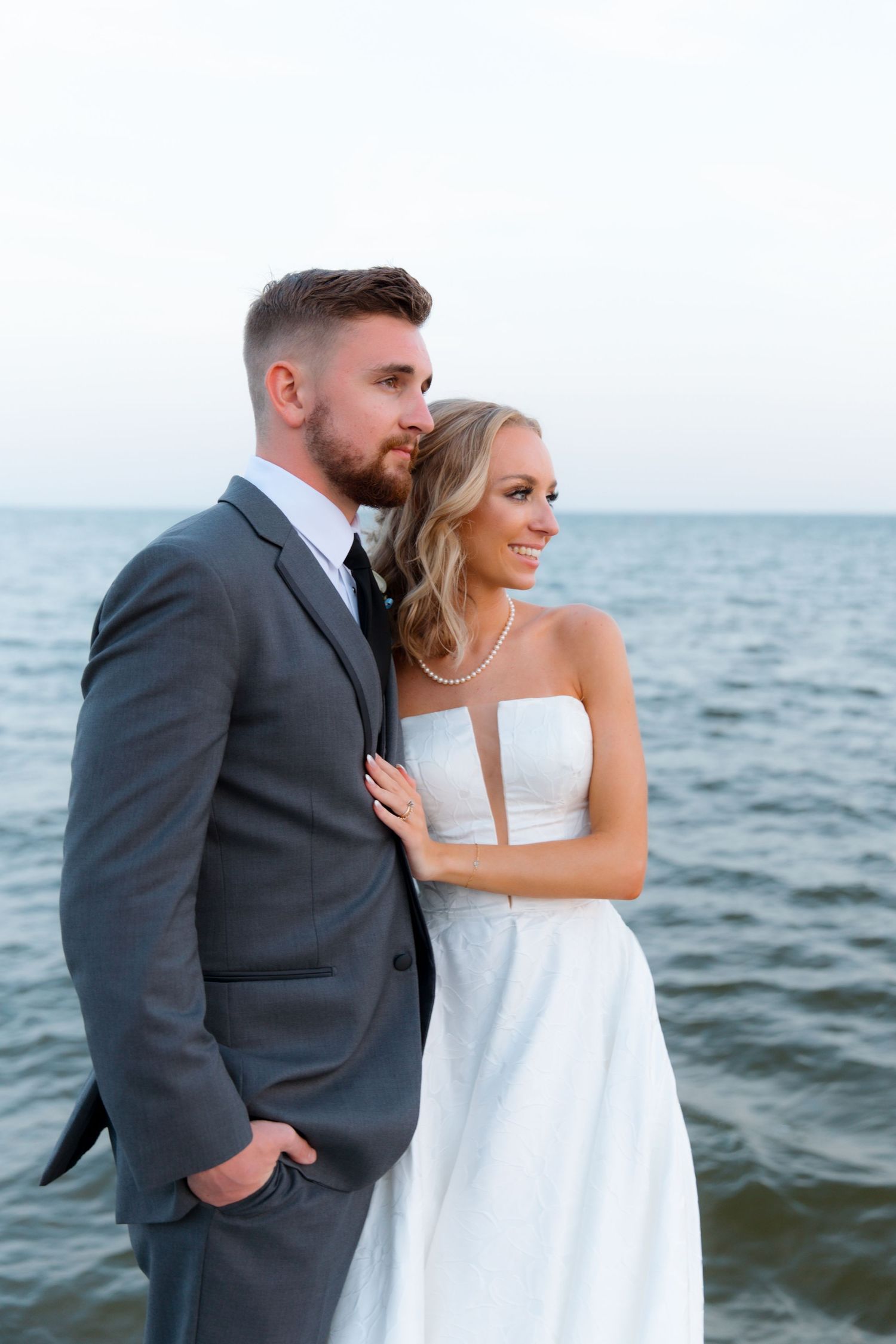 Couple embraces on a waterfront dock with ocean waves in the background.