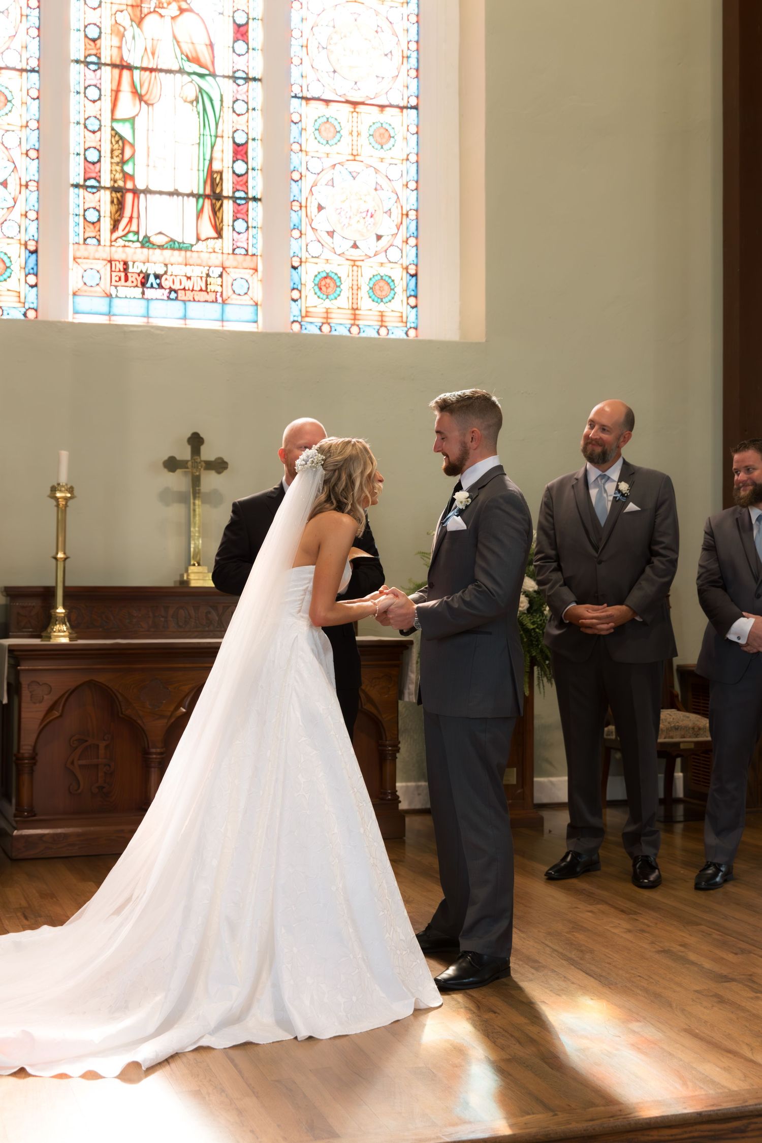 Bride and groom exchange vows in a church with stained glass windows and wooden altar.