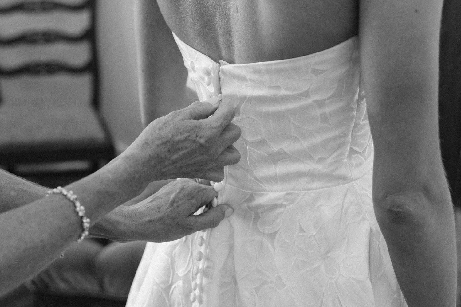 Close-up of hands adjusting the back of a white wedding dress.