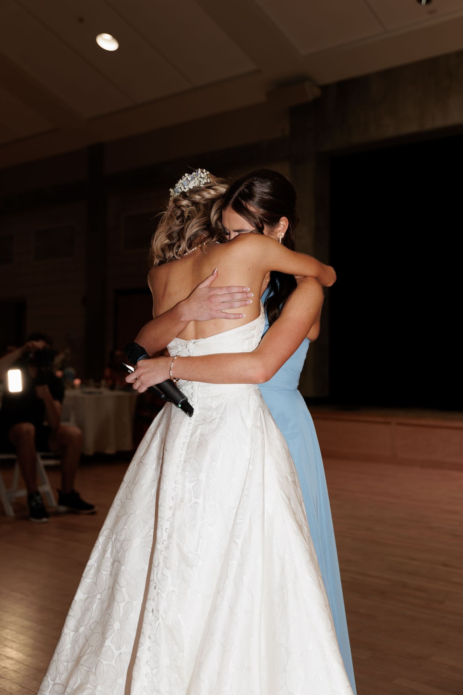 Emotional embrace between two women in formal dresses during wedding reception.