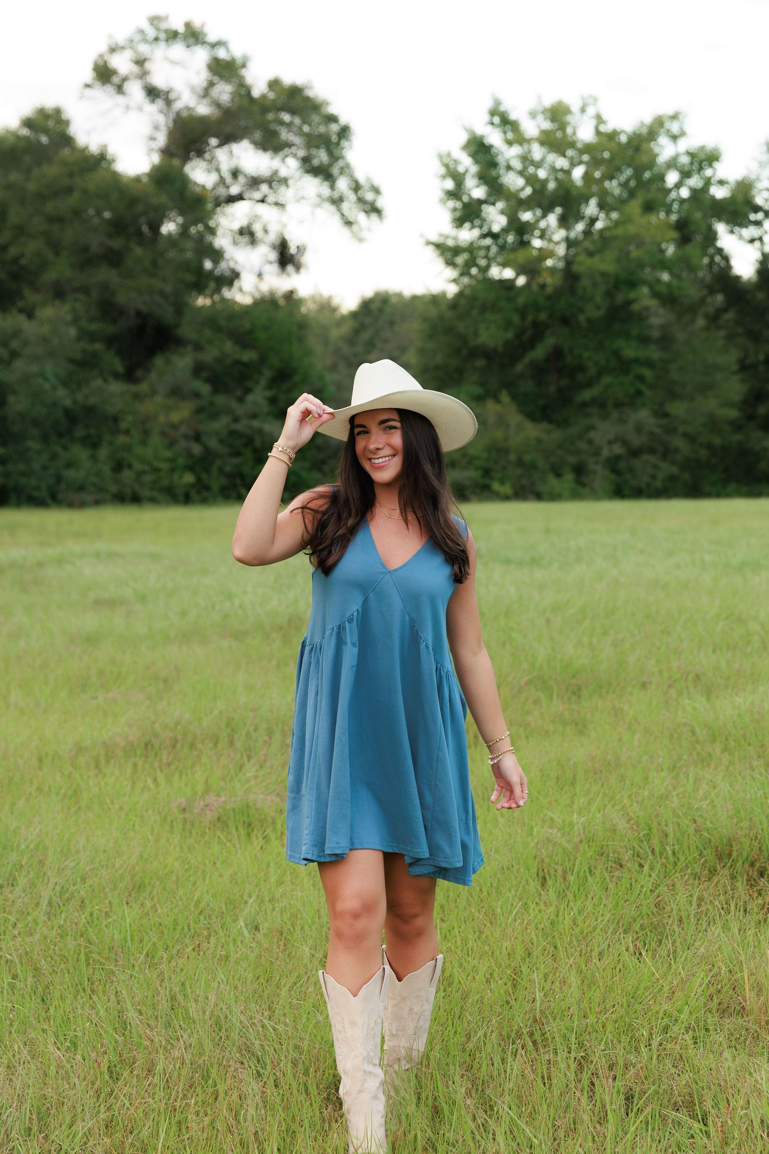 Woman in blue dress and cowboy boots poses in rustic field setting.