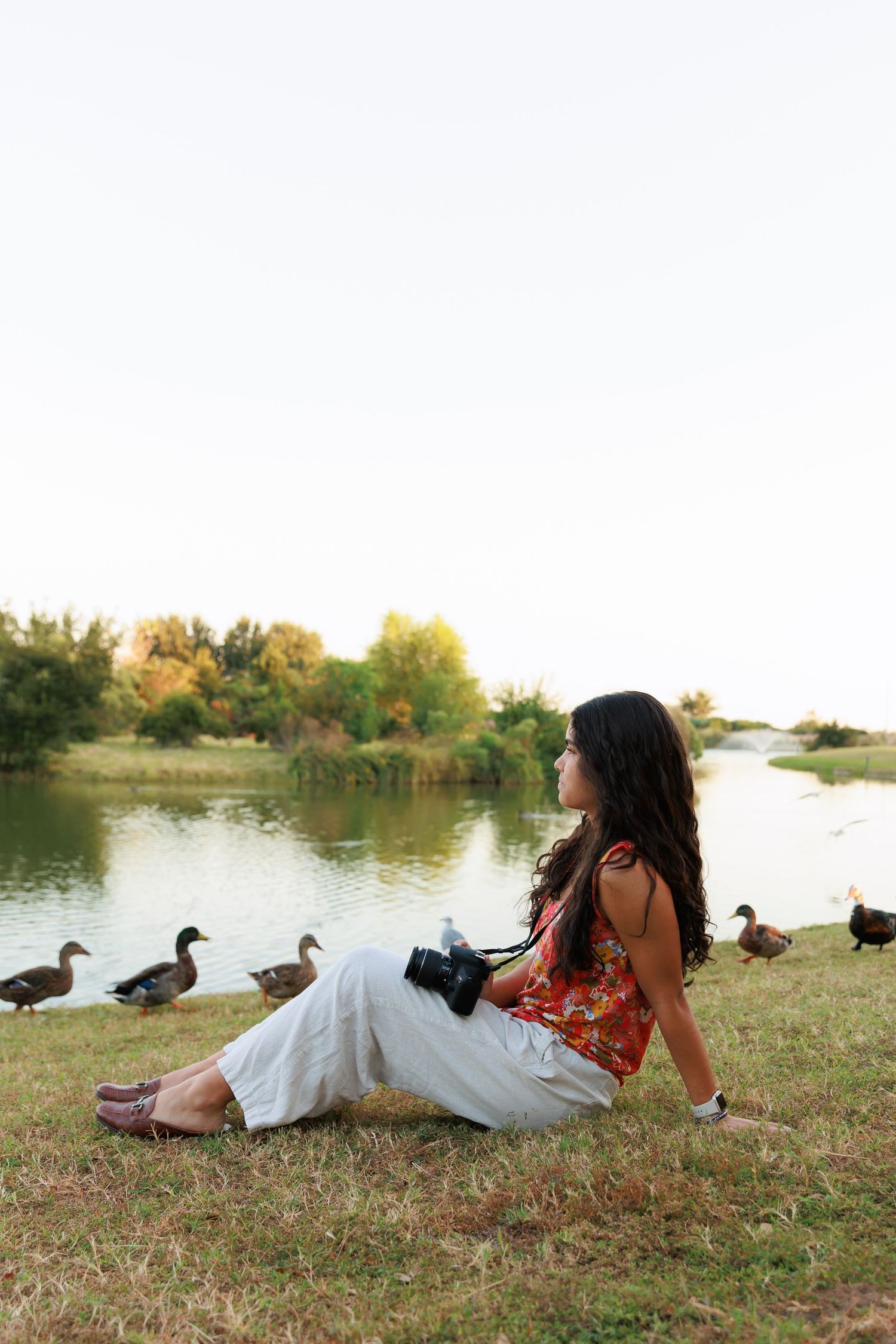 Peaceful lakeside moment with ducks and photographer resting on grassy bank.