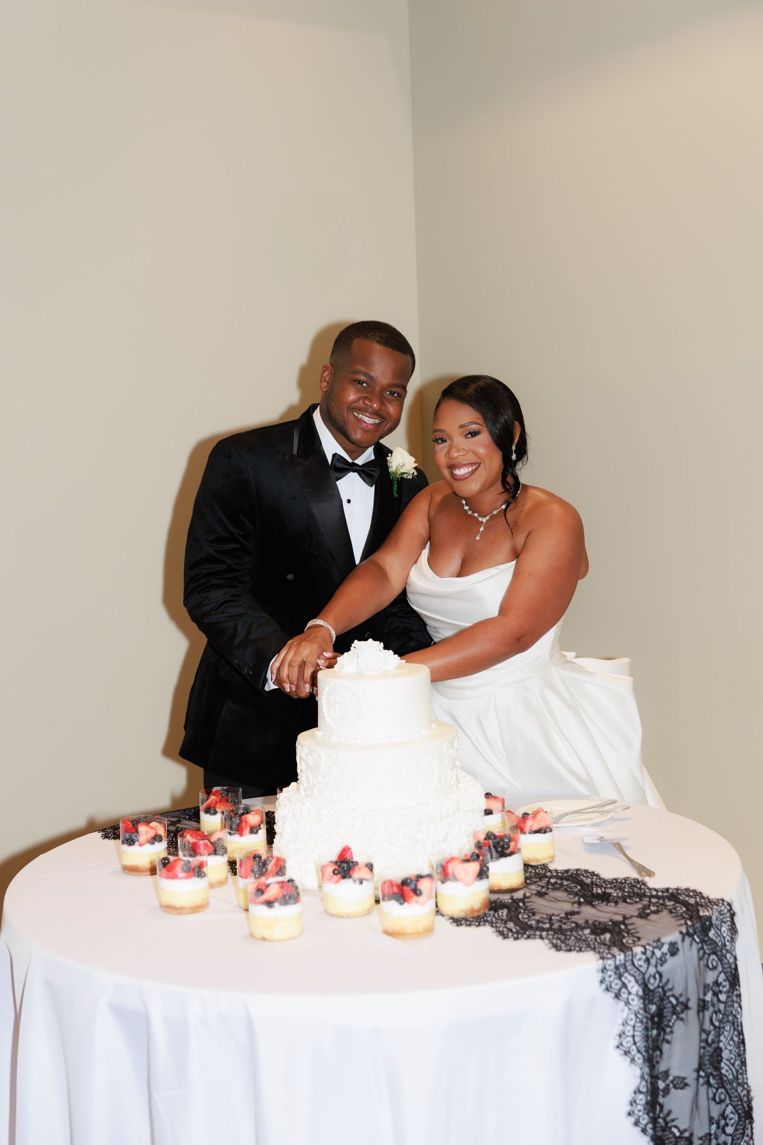 Newlyweds pose playfully with cupcakes on decorated table at their reception.