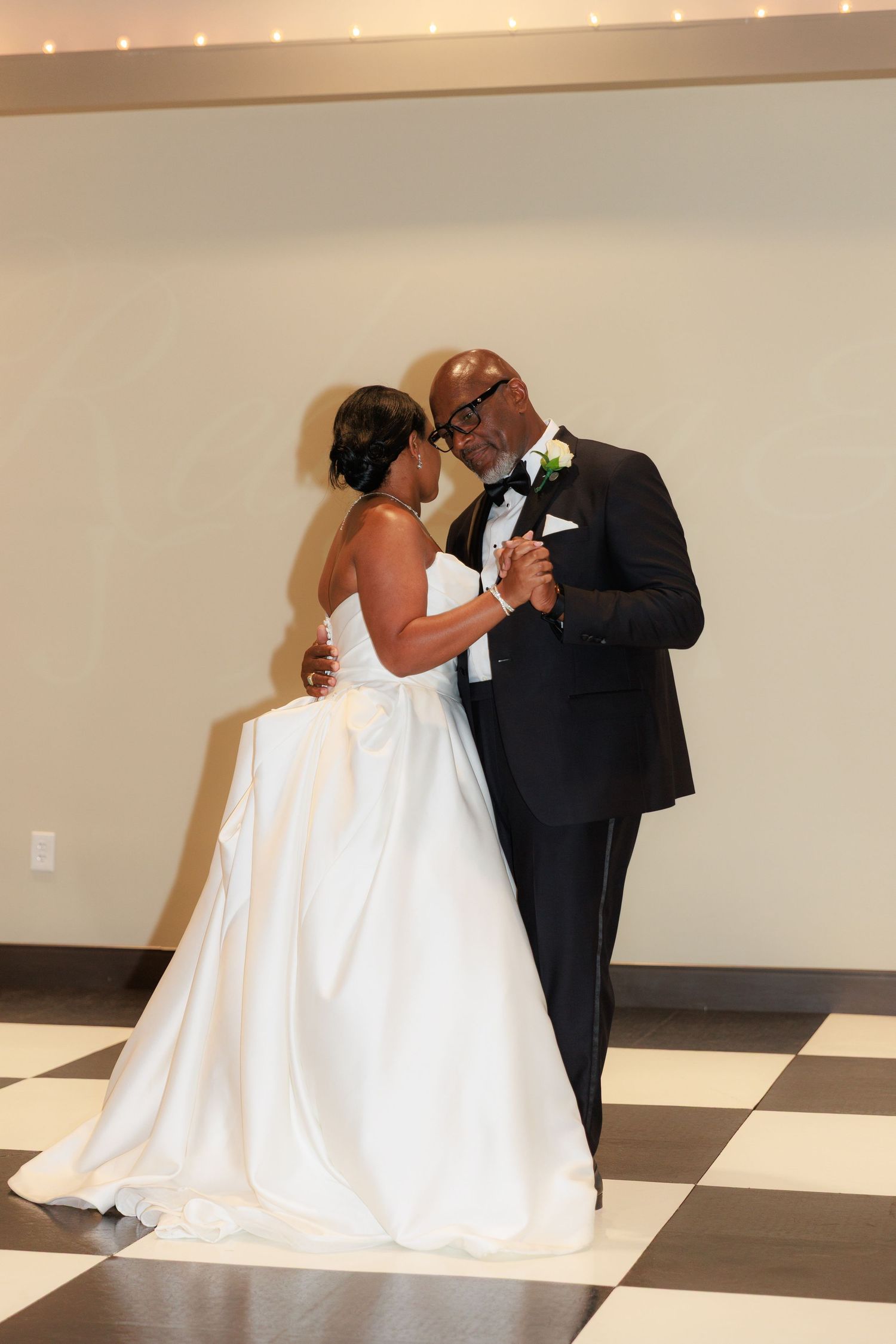 A romantic first dance between newlyweds on a black and white checkered floor at their wedding reception.