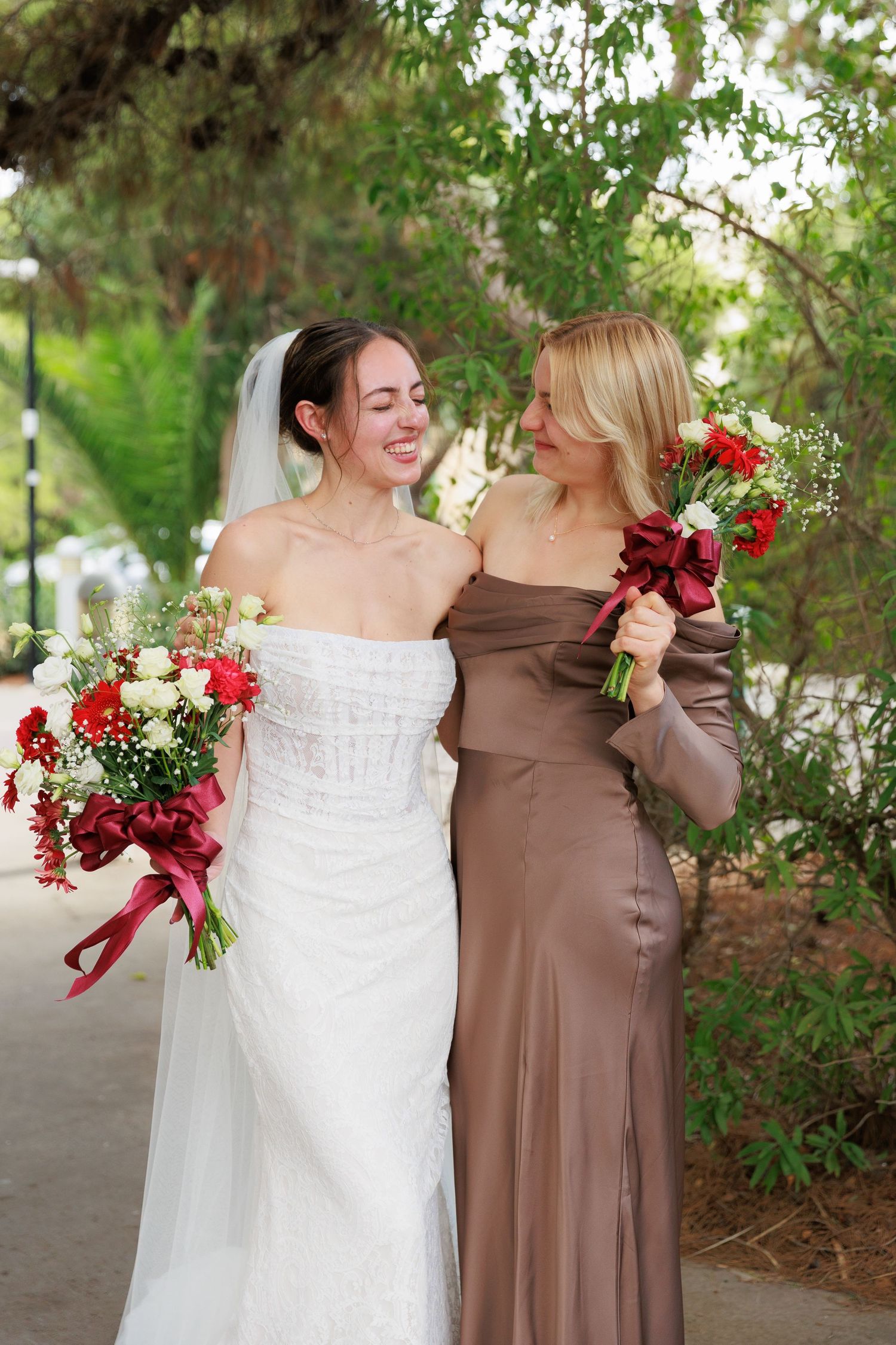 Wedding party members in brown and white dresses share candid laughing moments together outdoors.