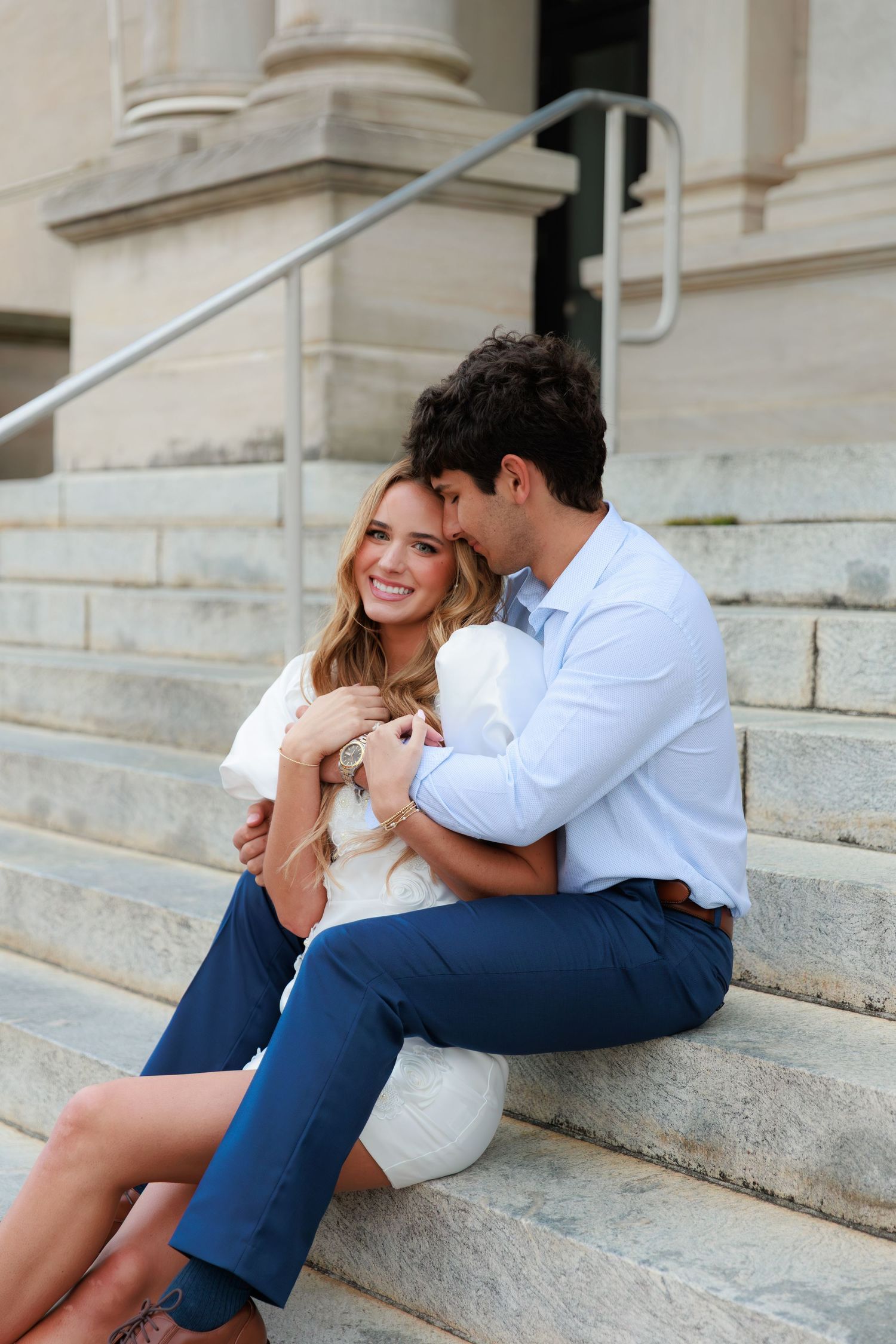 A couple sits close together and laughs while relaxing on stone steps outside a historic building.