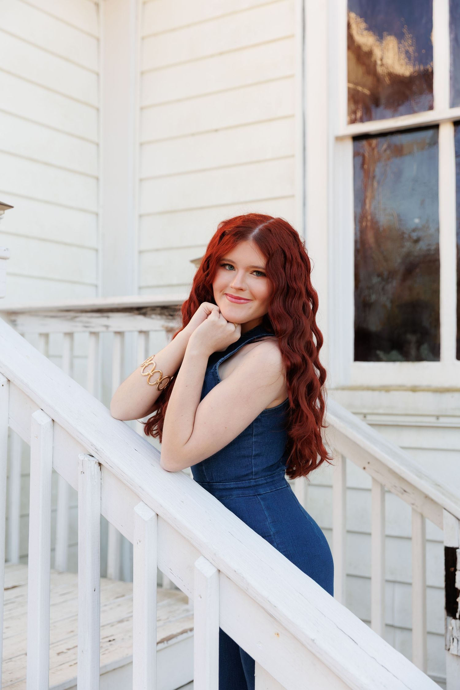 Woman in navy blue outfit poses against white porch railing at sunset.
