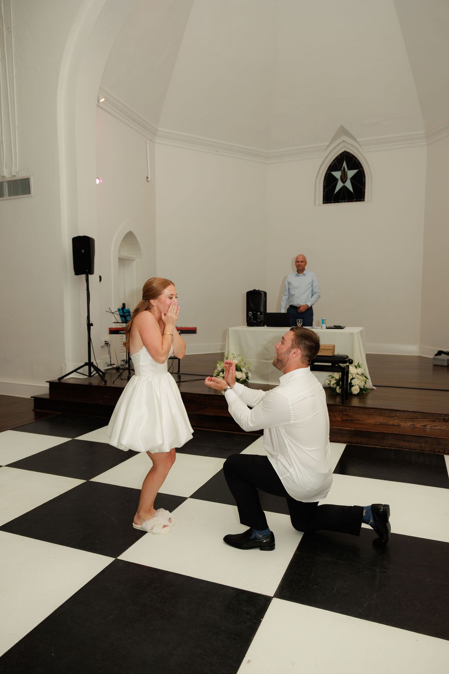 Groom kneeling on one knee before bride on black and white dance floor during wedding first dance.