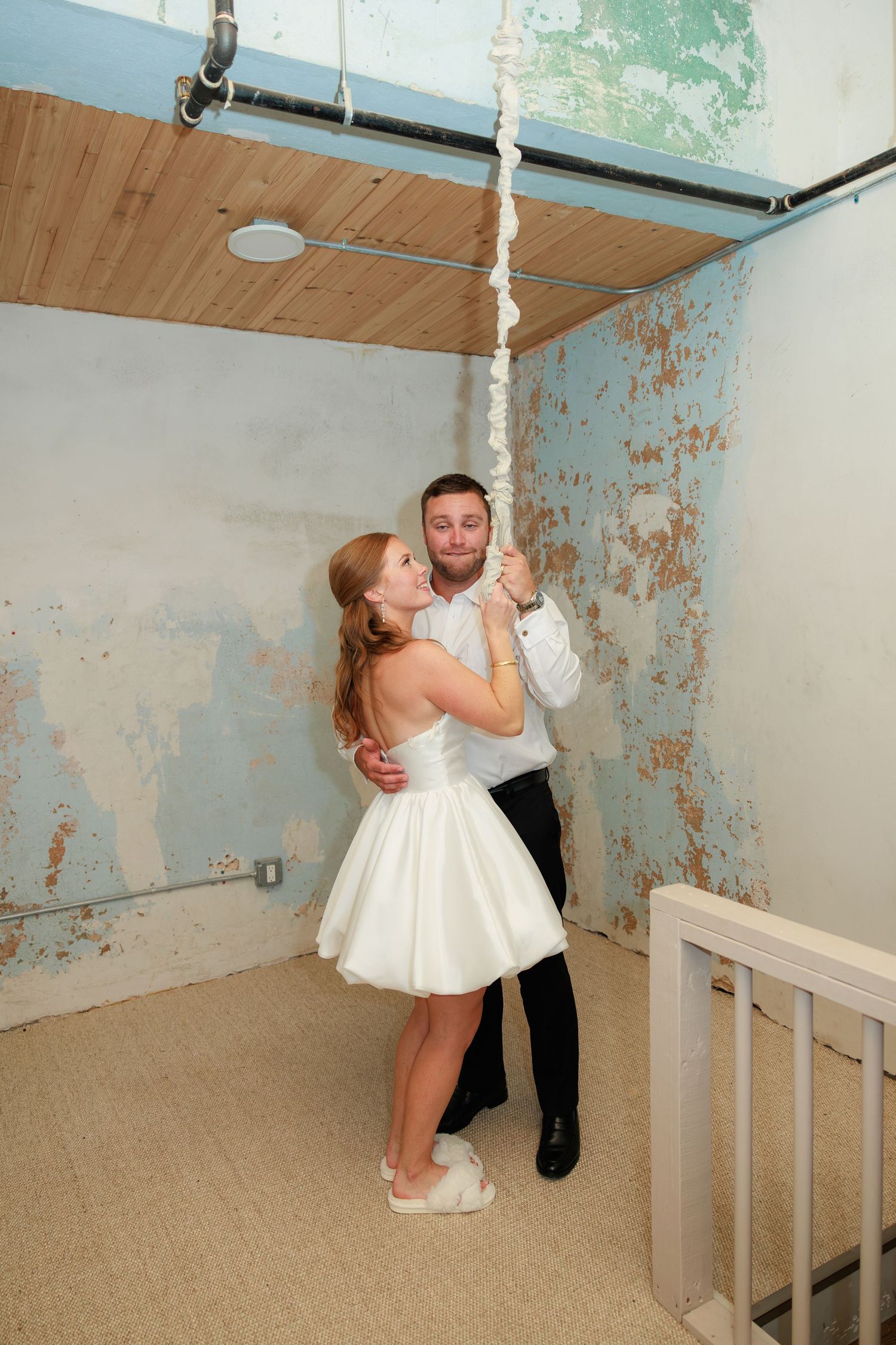Bride and groom share a romantic dance in a rustic room with peeling blue walls, she wearing a short white dress.