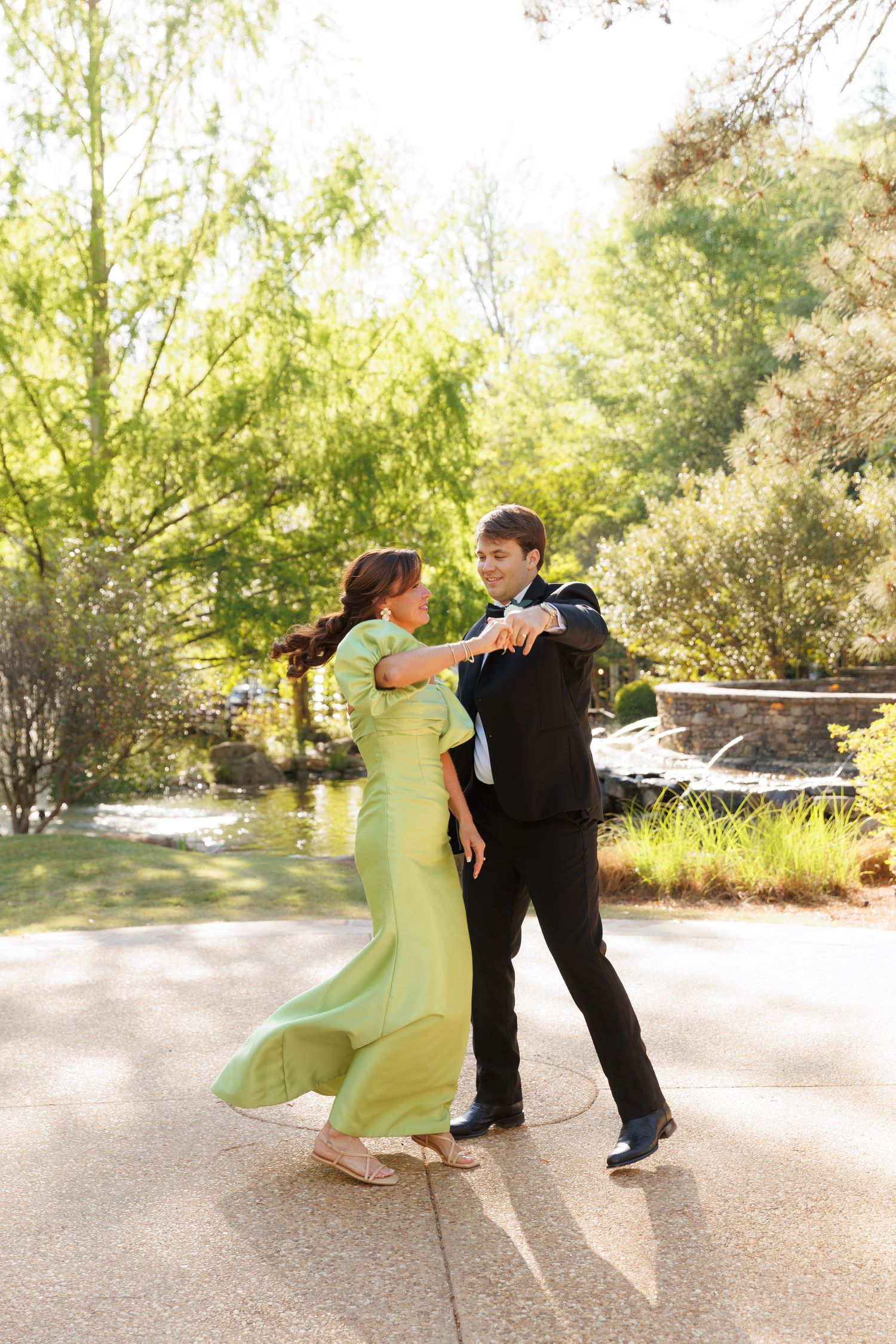 Couple dancing outdoors in a garden, woman in flowing green gown and man in black tuxedo.