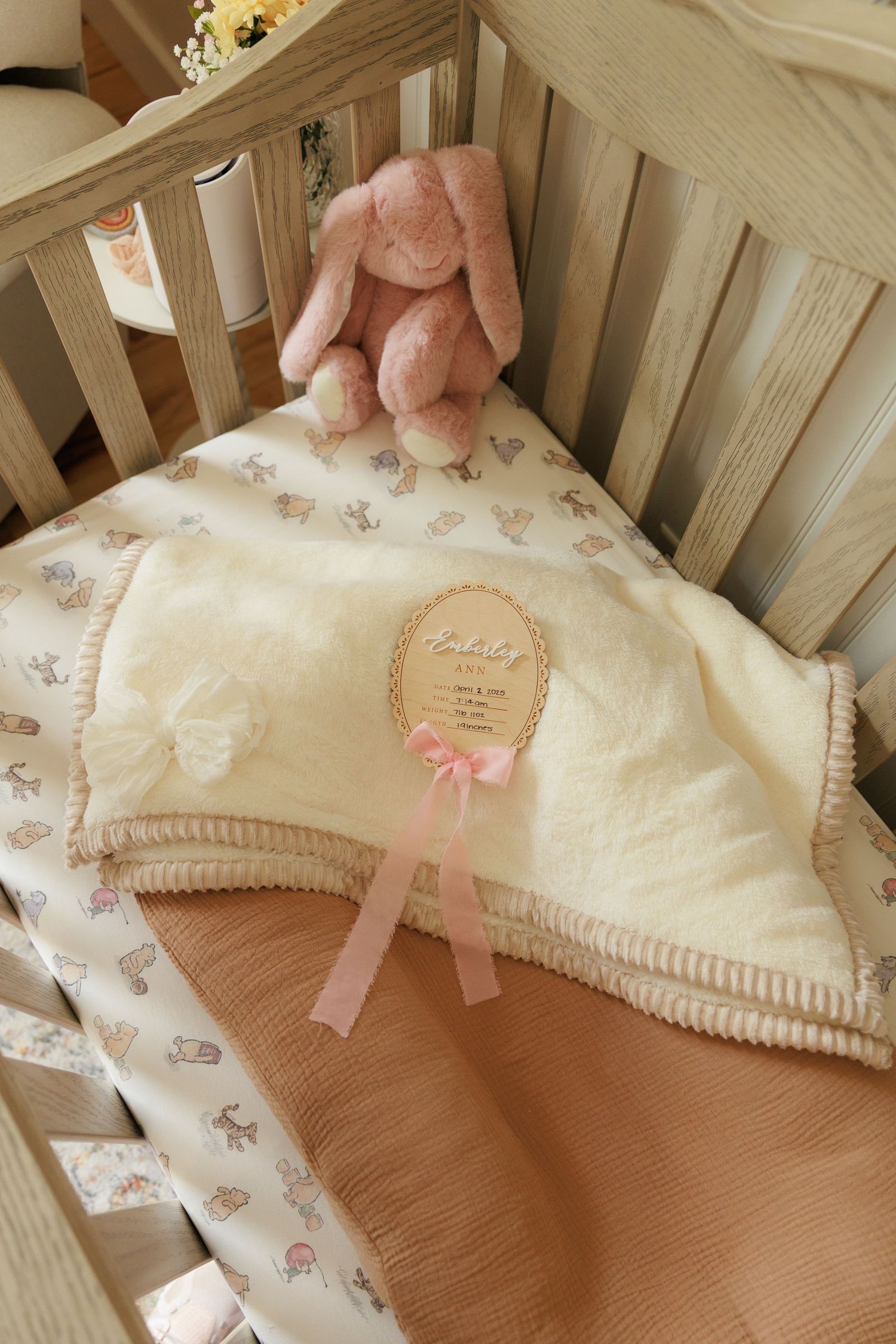 A white baby crib with delicate floral bedding and pink ribbon accents shown from multiple angles.