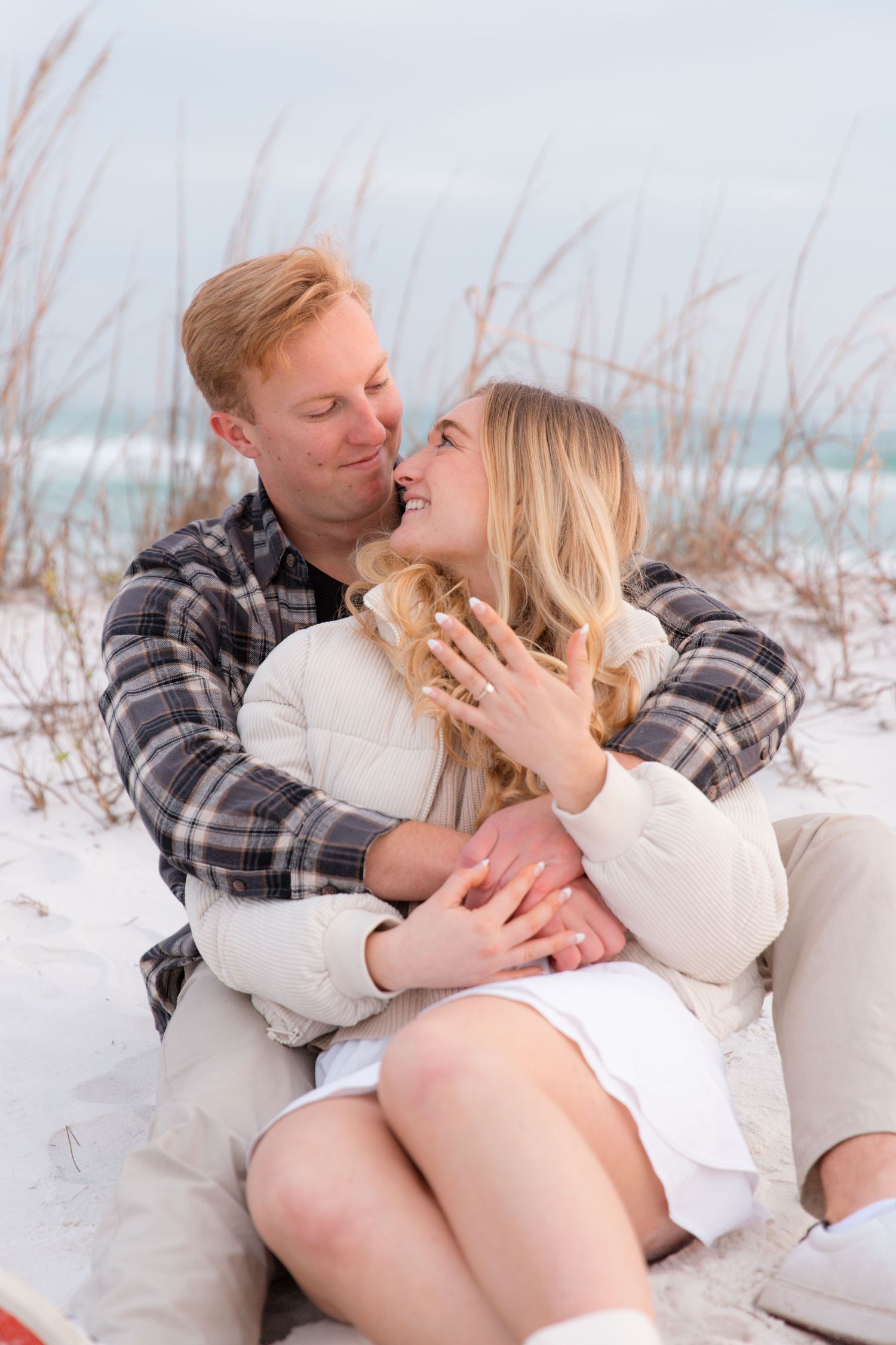 Romantic couple sitting together on white sand beach sharing intimate moments at sunset.
