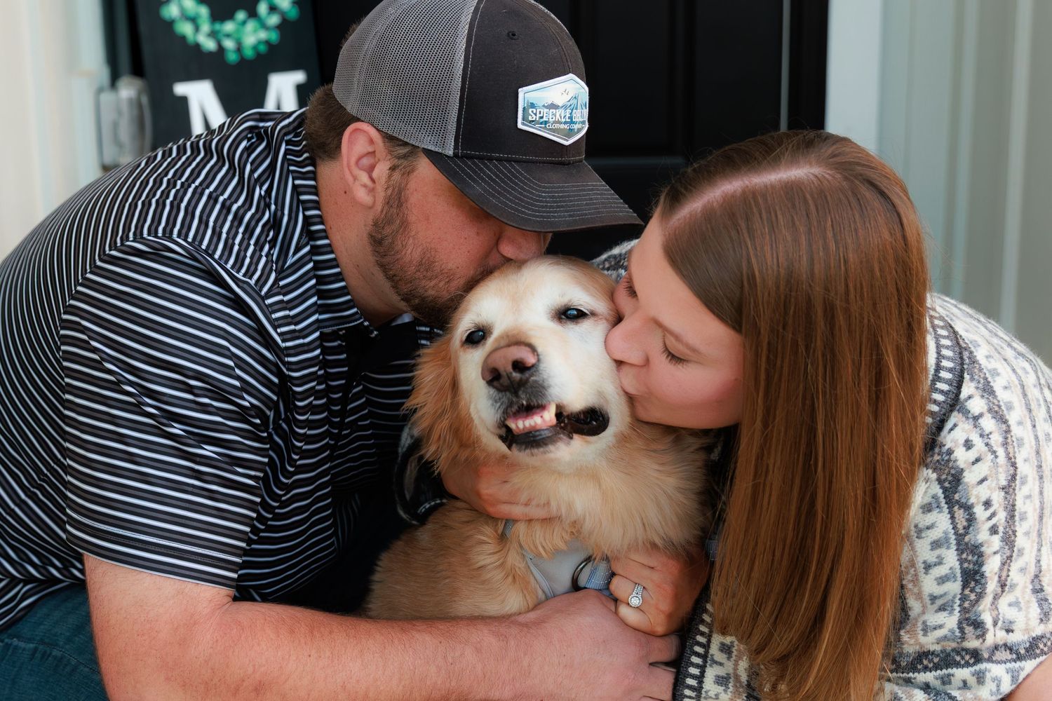 A fluffy tan and white dog receives affection and cuddles from two people in a heartwarming moment.