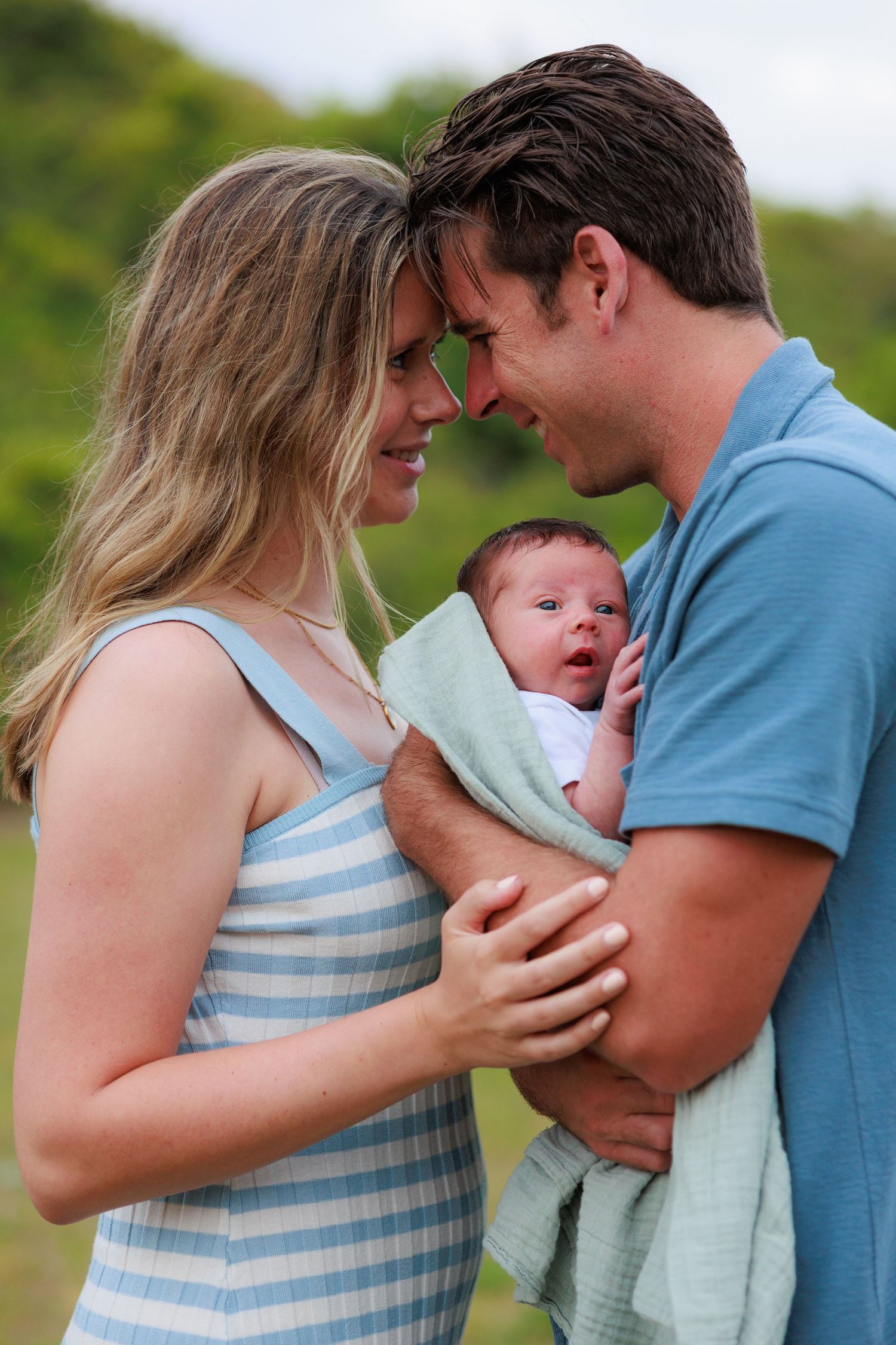 A couple cradles their newborn baby outdoors while sharing tender family moments together.
