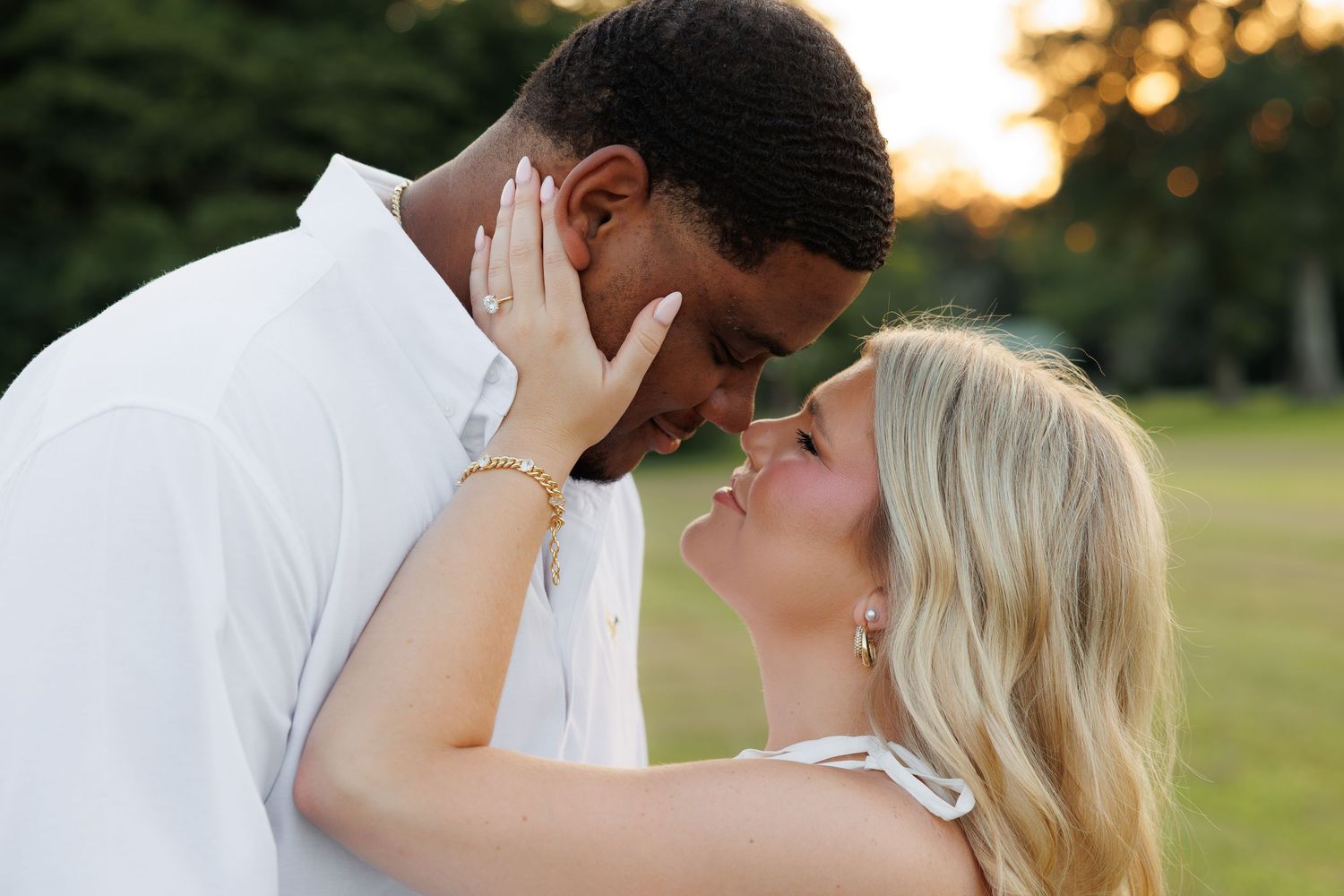 Romantic interracial couple sharing an intimate moment at golden hour in a lush green park.