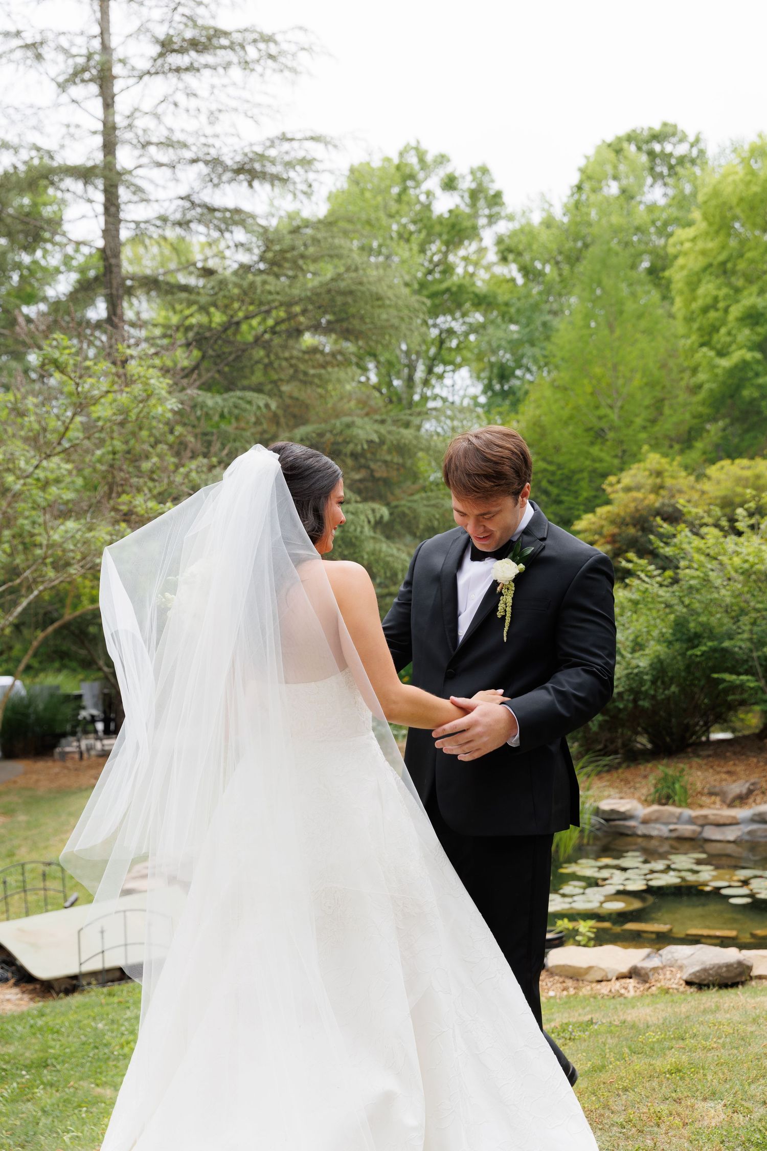 Bride and groom share tender moment holding hands in lush garden setting during wedding first look.