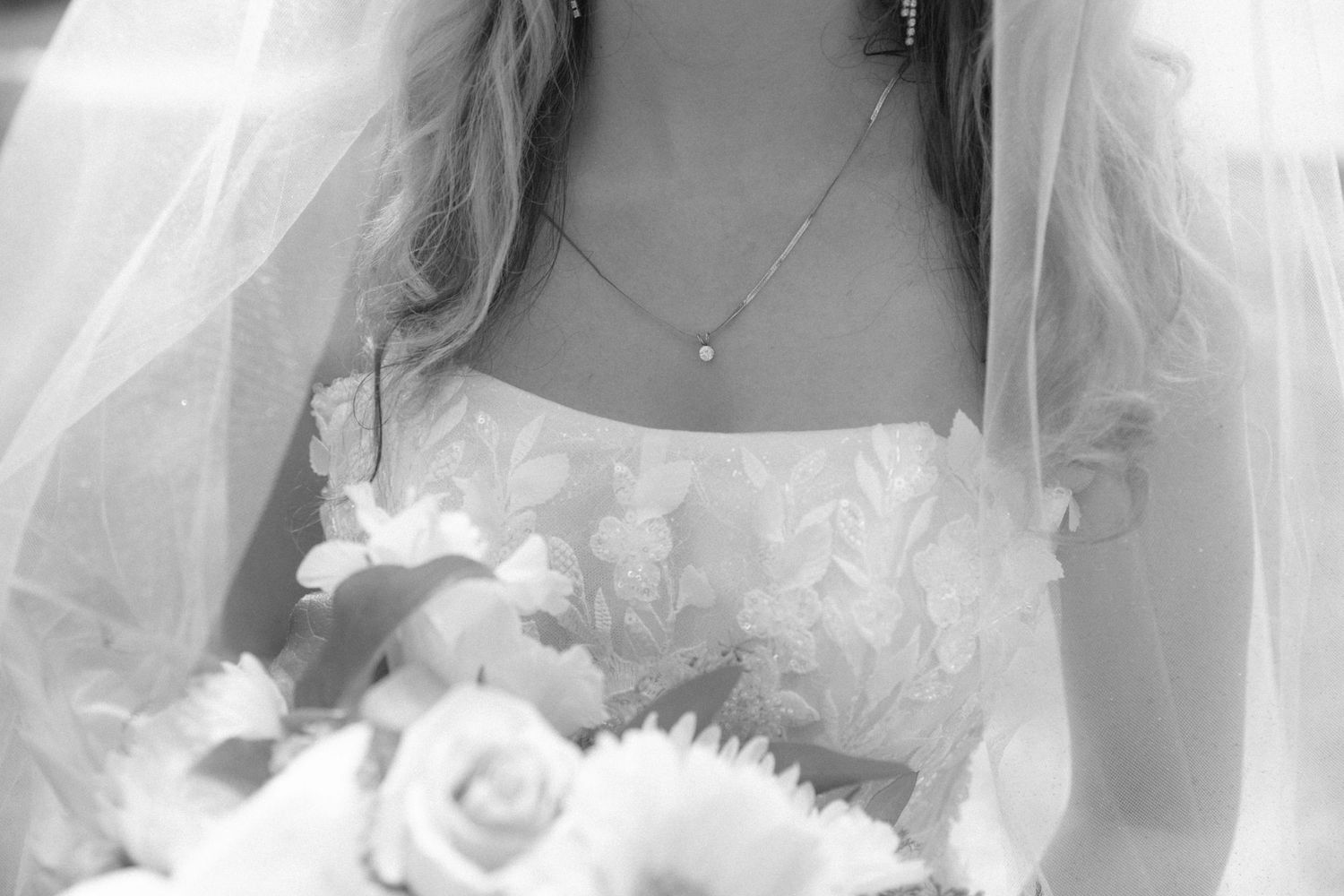A bride in a white wedding dress holds a bouquet of flowers while posing against a light background.