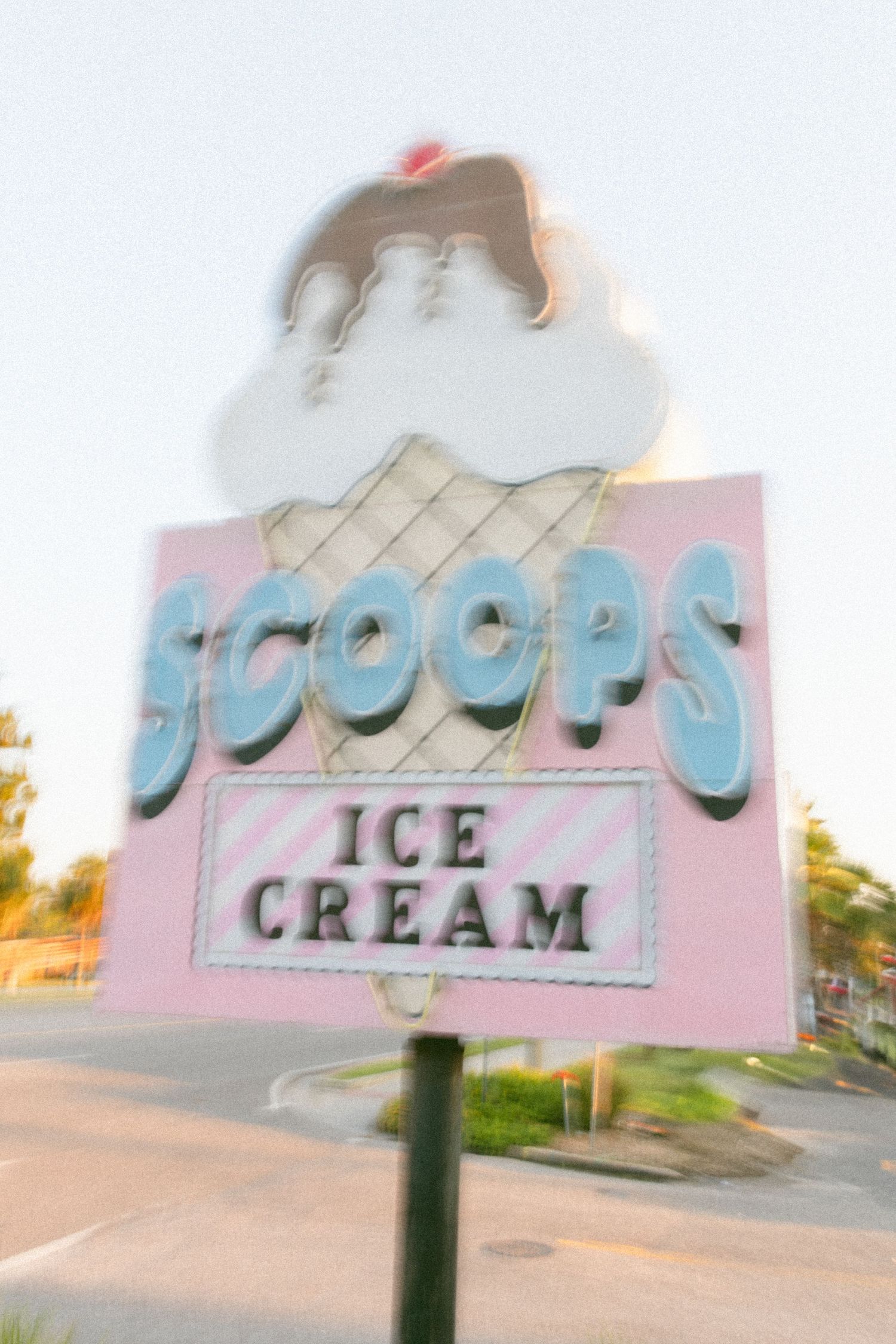 A retro pink and blue ice cream shop sign with vintage styling photographed at dusk.