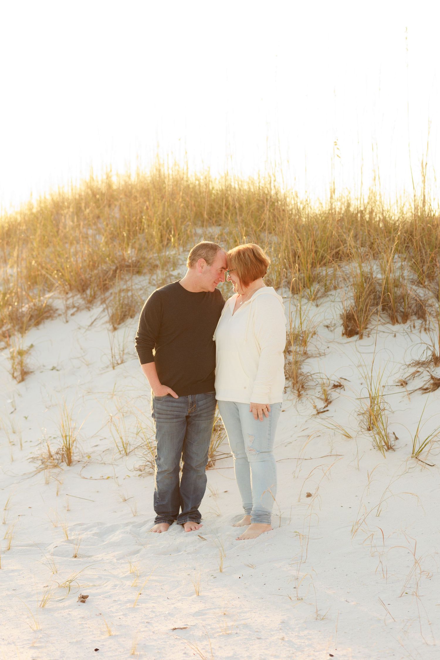 A couple shares an intimate moment on sandy dunes at sunset with warm golden lighting.