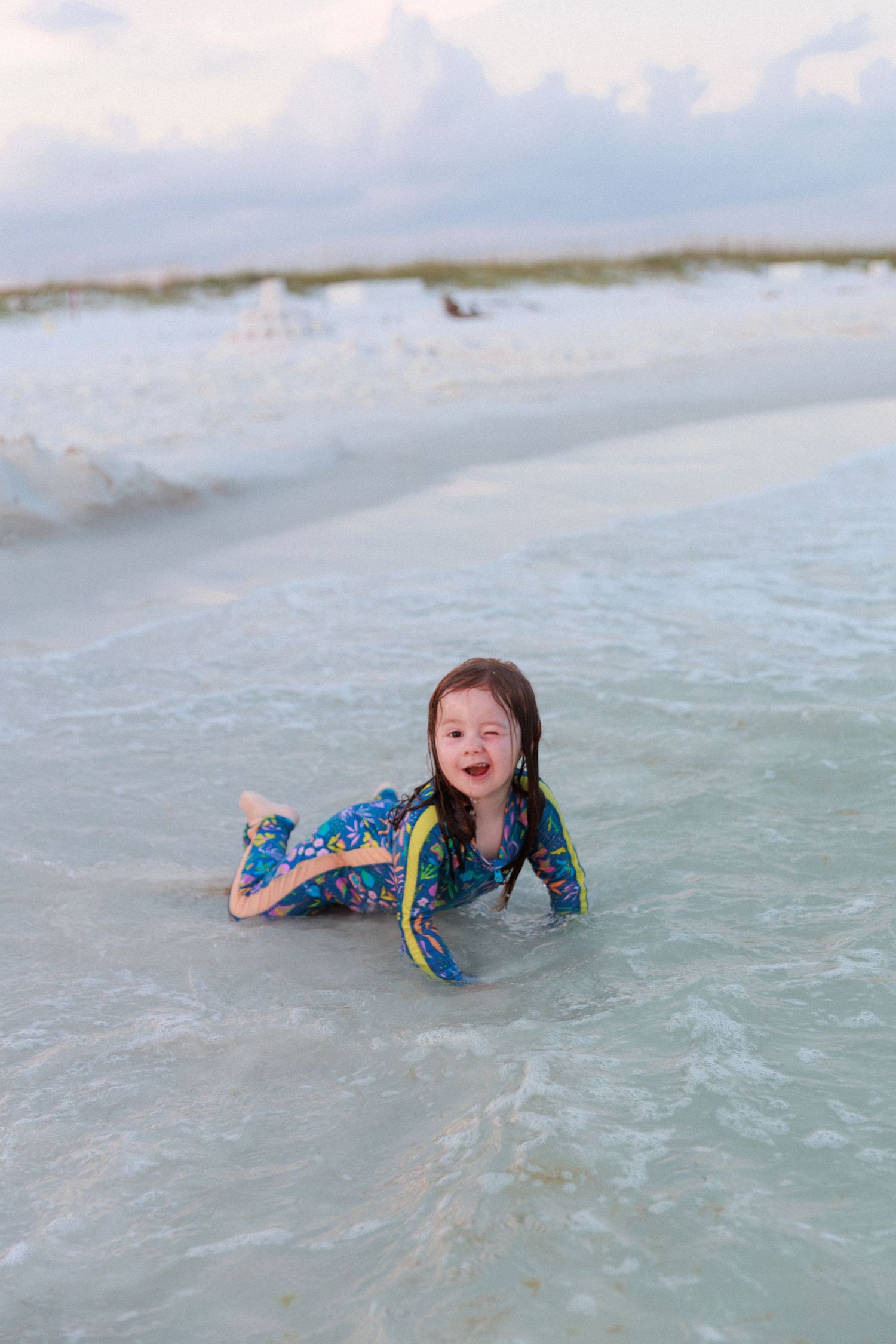 Child playing and splashing in shallow ocean waves wearing blue swim clothing.