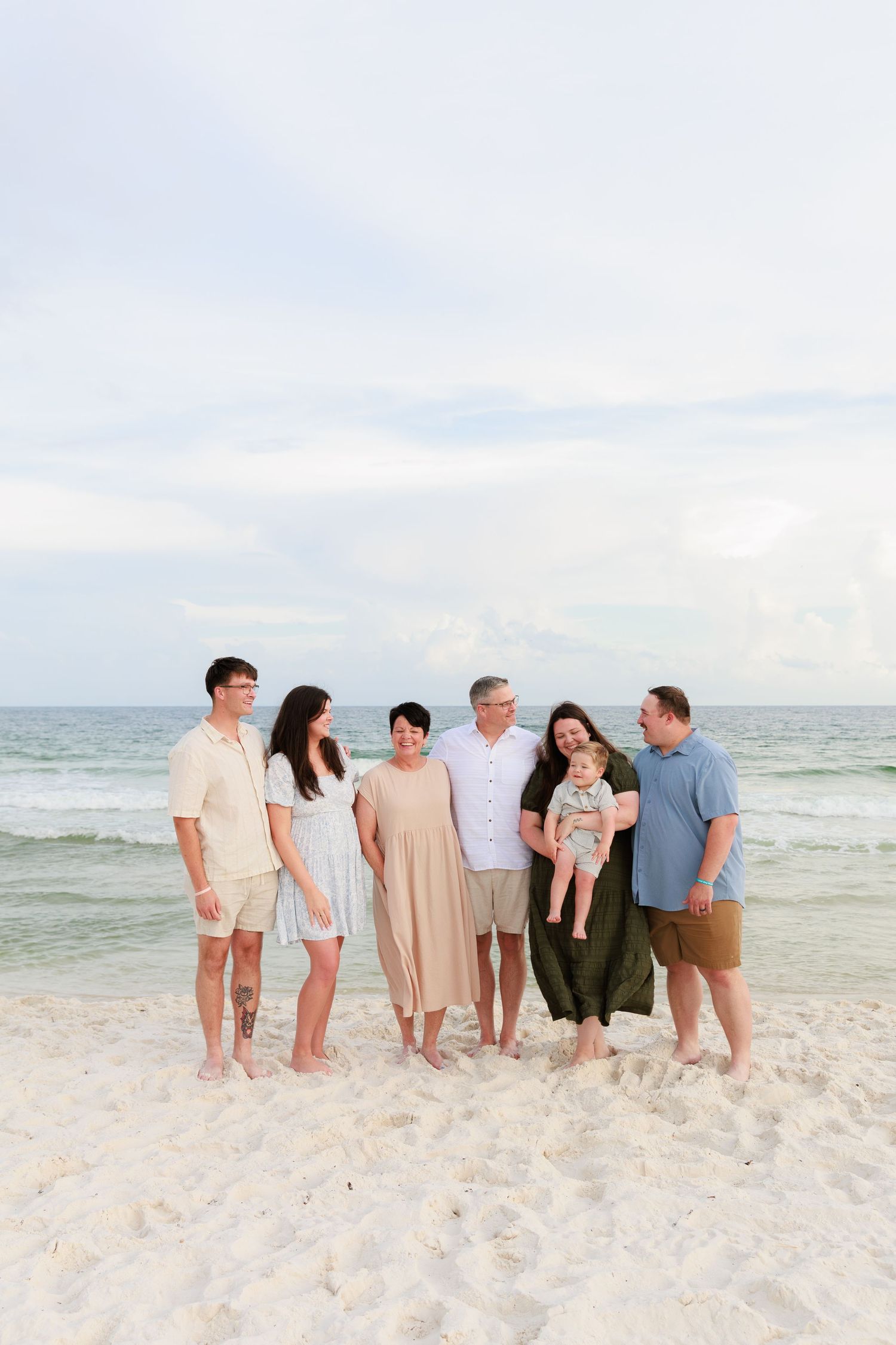 A group of people standing together on a white sandy beach with the ocean and cloudy sky in the background.