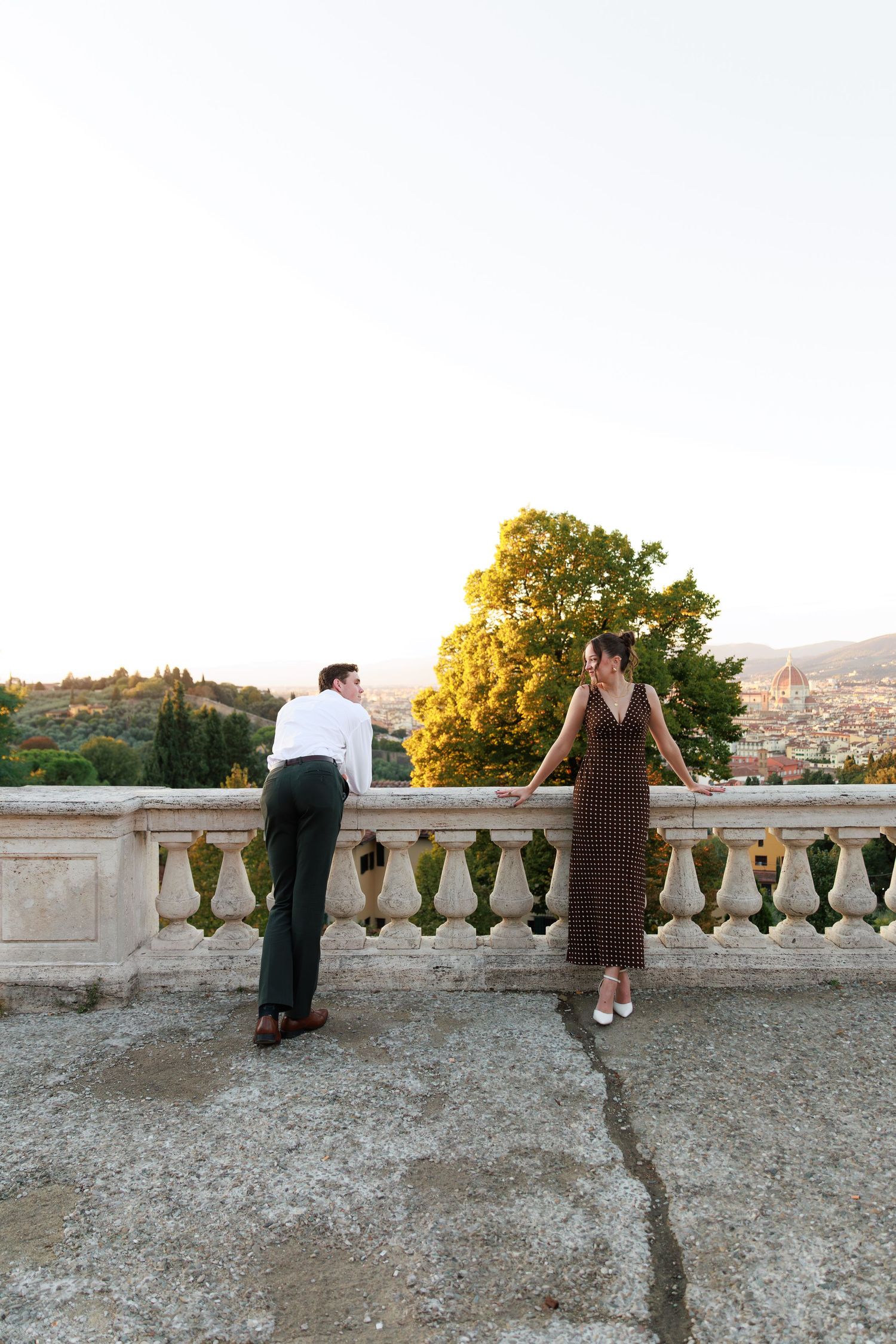 Couple enjoying sunset views from a classic stone balcony terrace overlooking Florence, Italy.