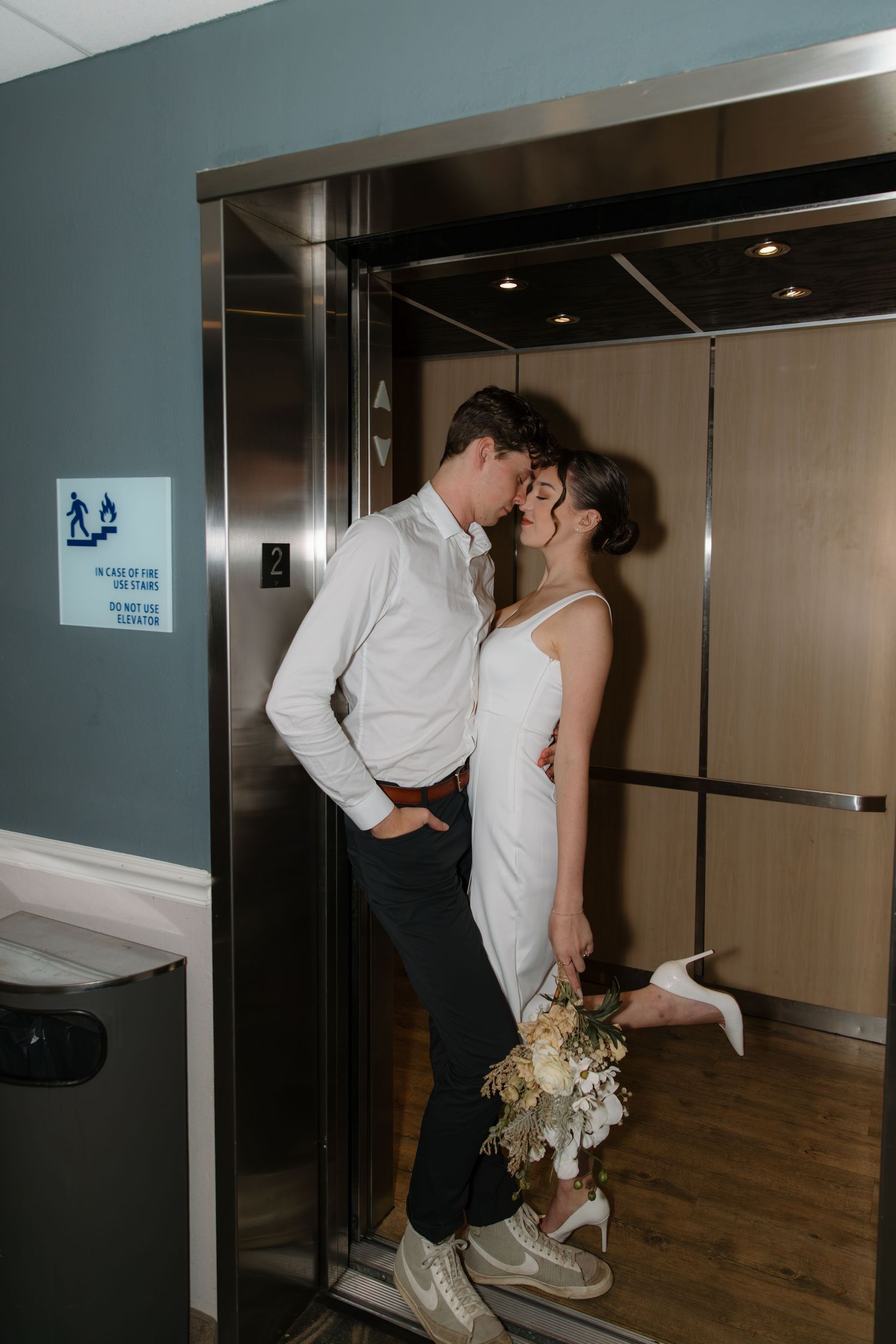 A couple in wedding attire share an intimate moment in an elevator during their special day.