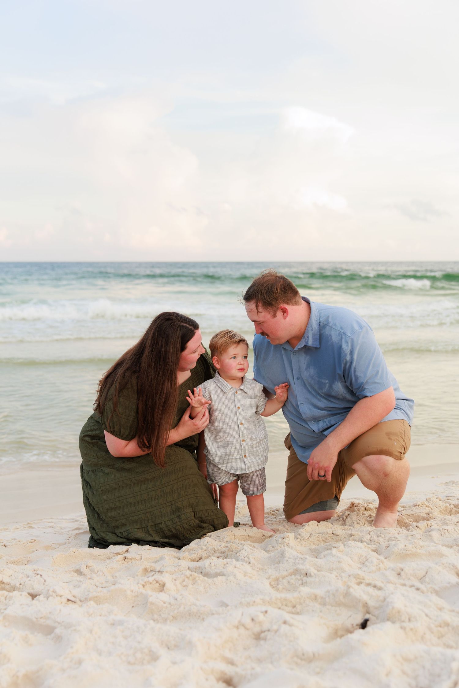 Family plays together on white sandy beach at sunset with ocean waves in background.