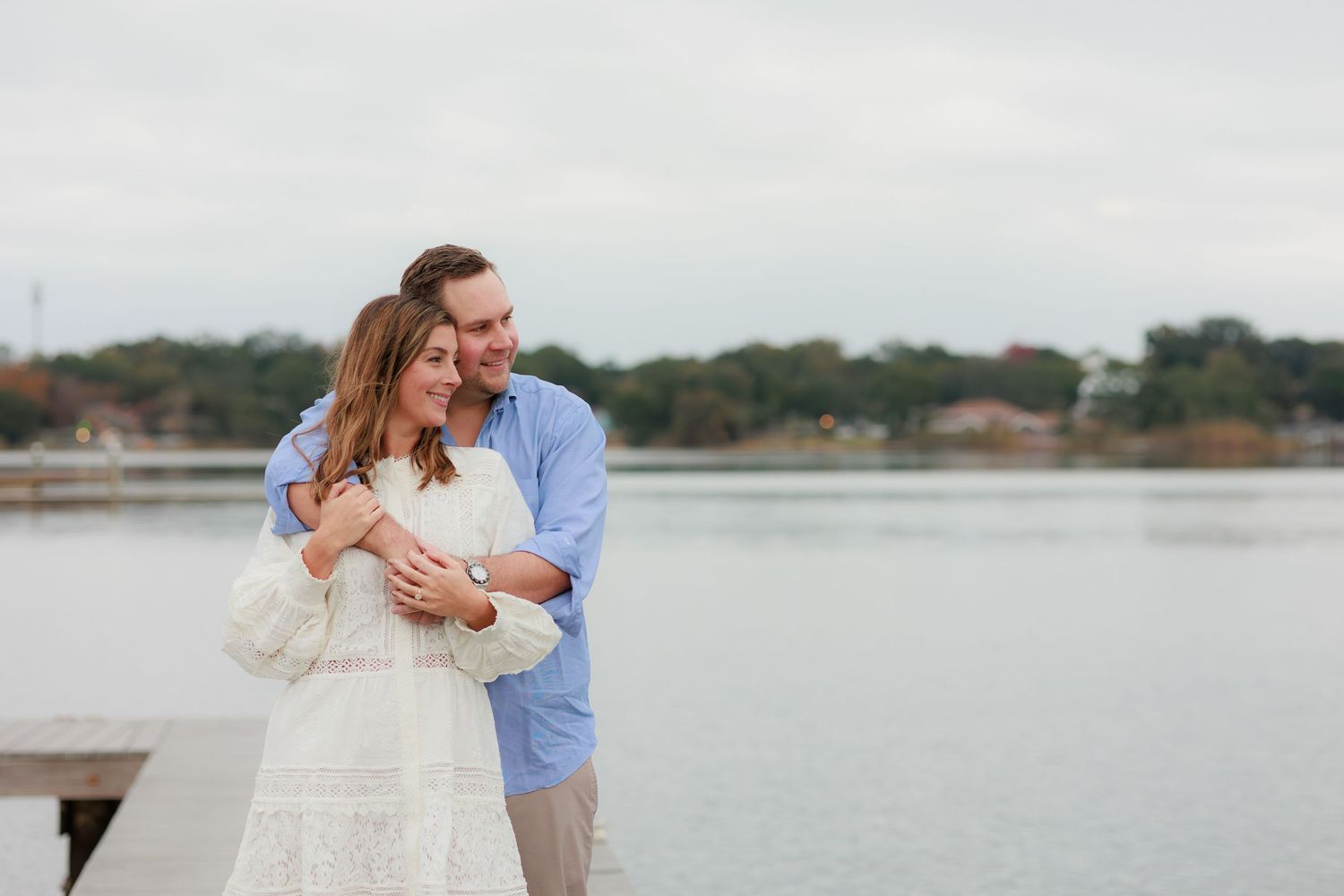 A couple embraces lovingly on a wooden dock overlooking a serene lake during a romantic photo session.