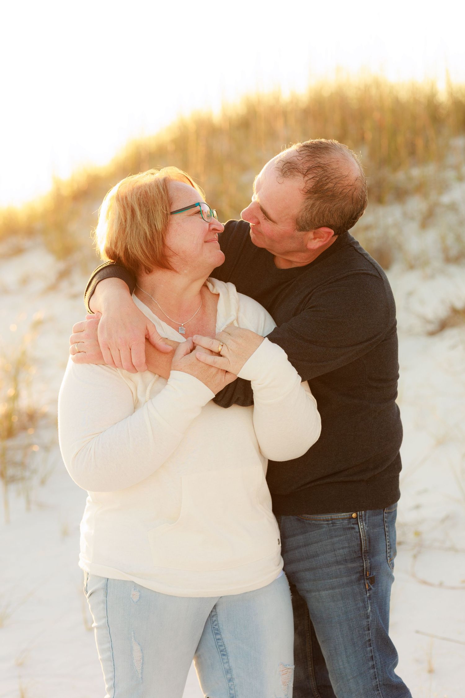 Tender moments captured between couple in white and black on beach at sunset.