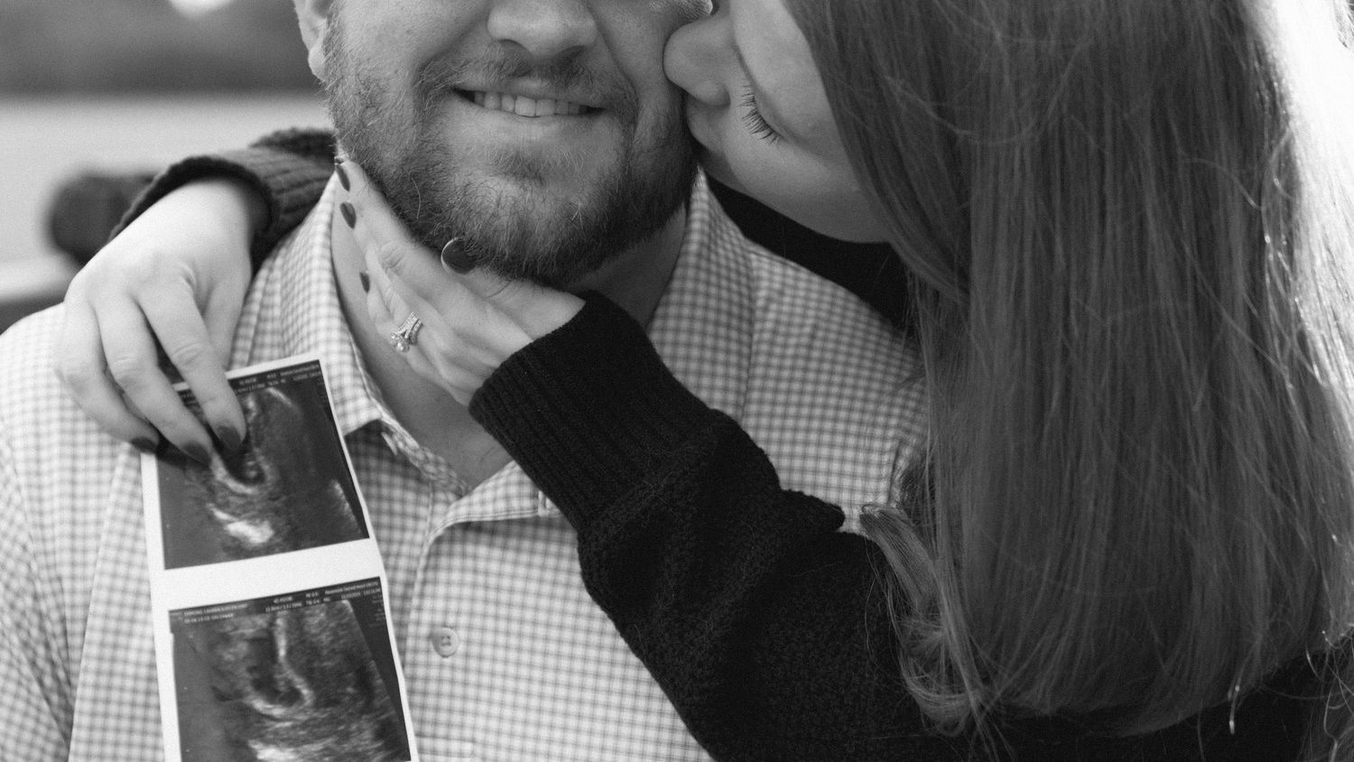A couple shares a tender moment while holding an ultrasound photo, announcing their pregnancy.