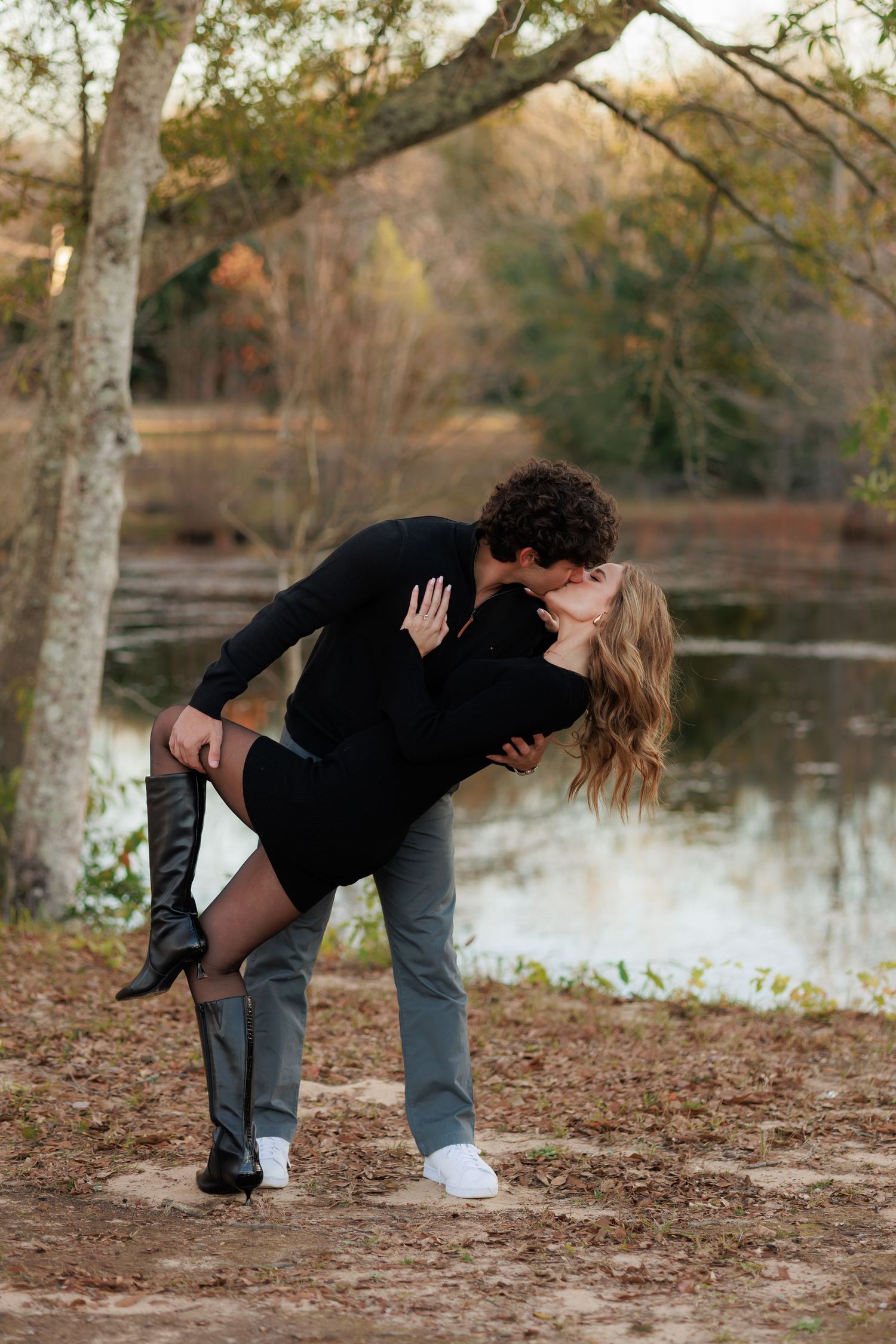 Romantic couple sharing an intimate moment by a lake during autumn with fall foliage in the background.
