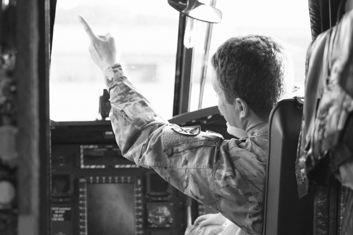 Black and white image of a pilot gesturing in a military aircraft cockpit.
