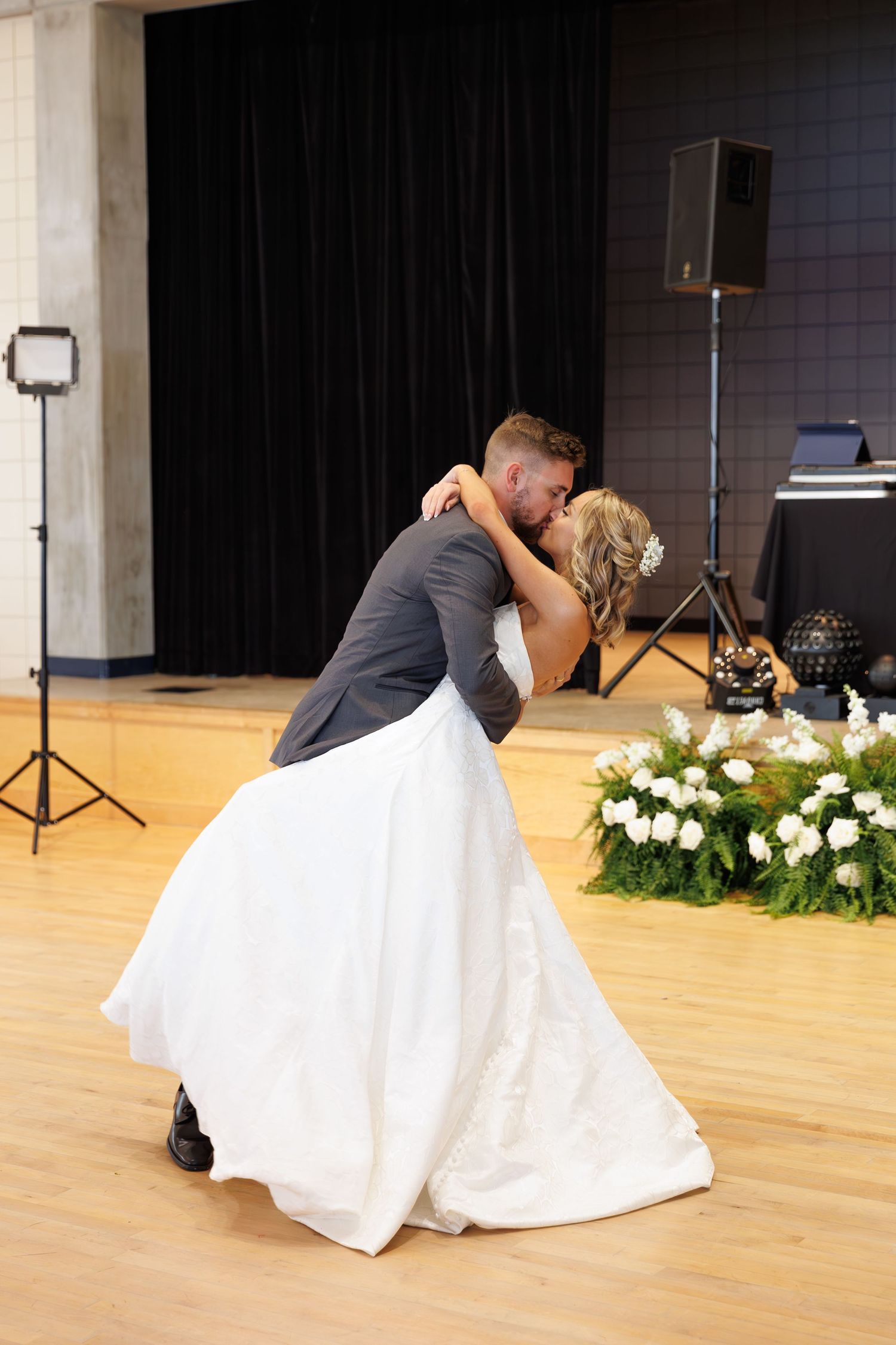 Romantic dance dip on hardwood floor during wedding reception with black curtain backdrop.