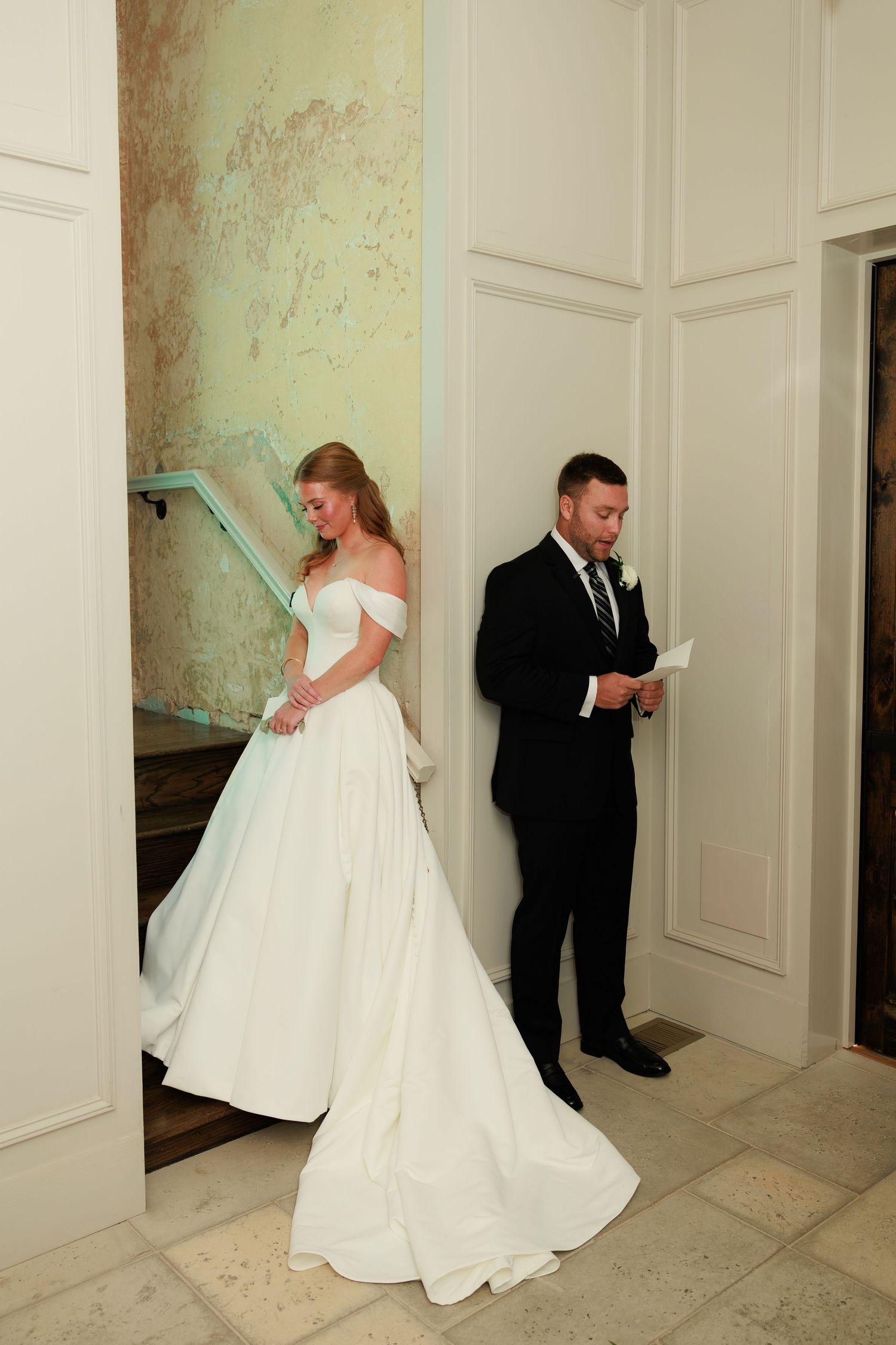 Bride in off-shoulder white ball gown and groom in black suit share a first look moment, reading vows separately.