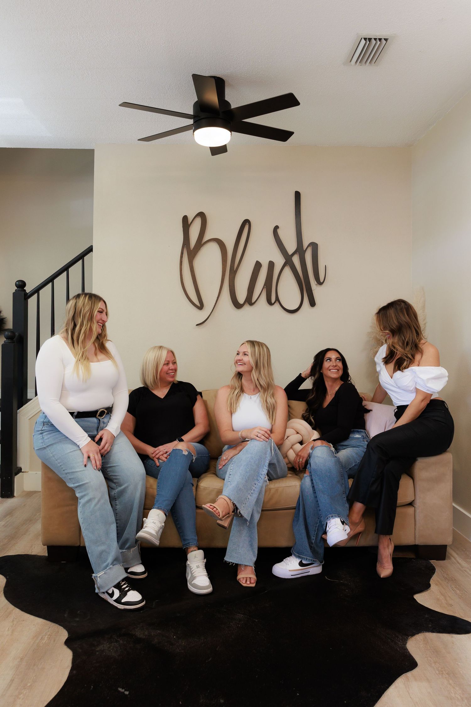 A group wearing jeans and black shirts pose casually on a black couch in a fun photo series.