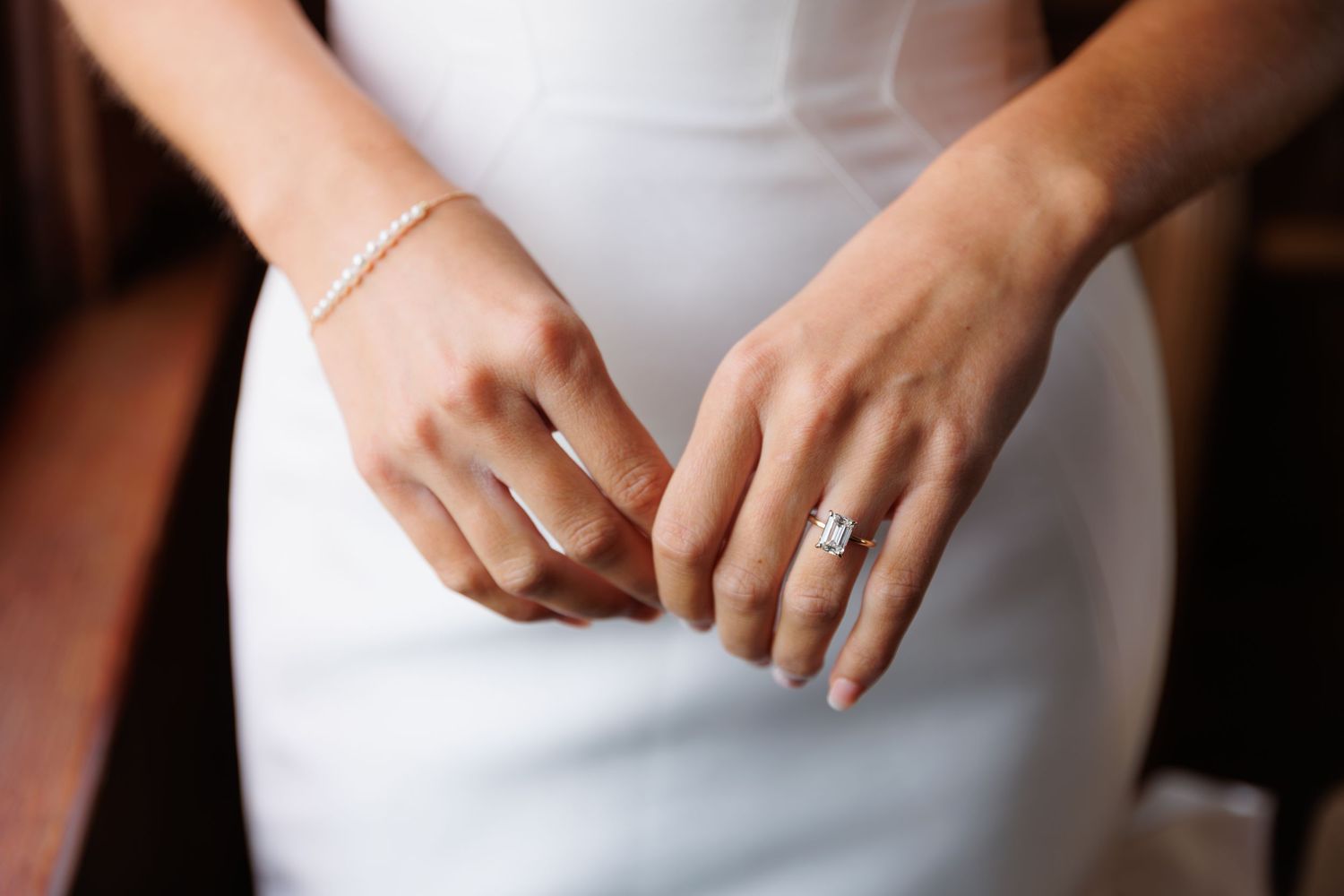 A close-up sequence of hands adjusting a white wedding dress with delicate details and fabric.