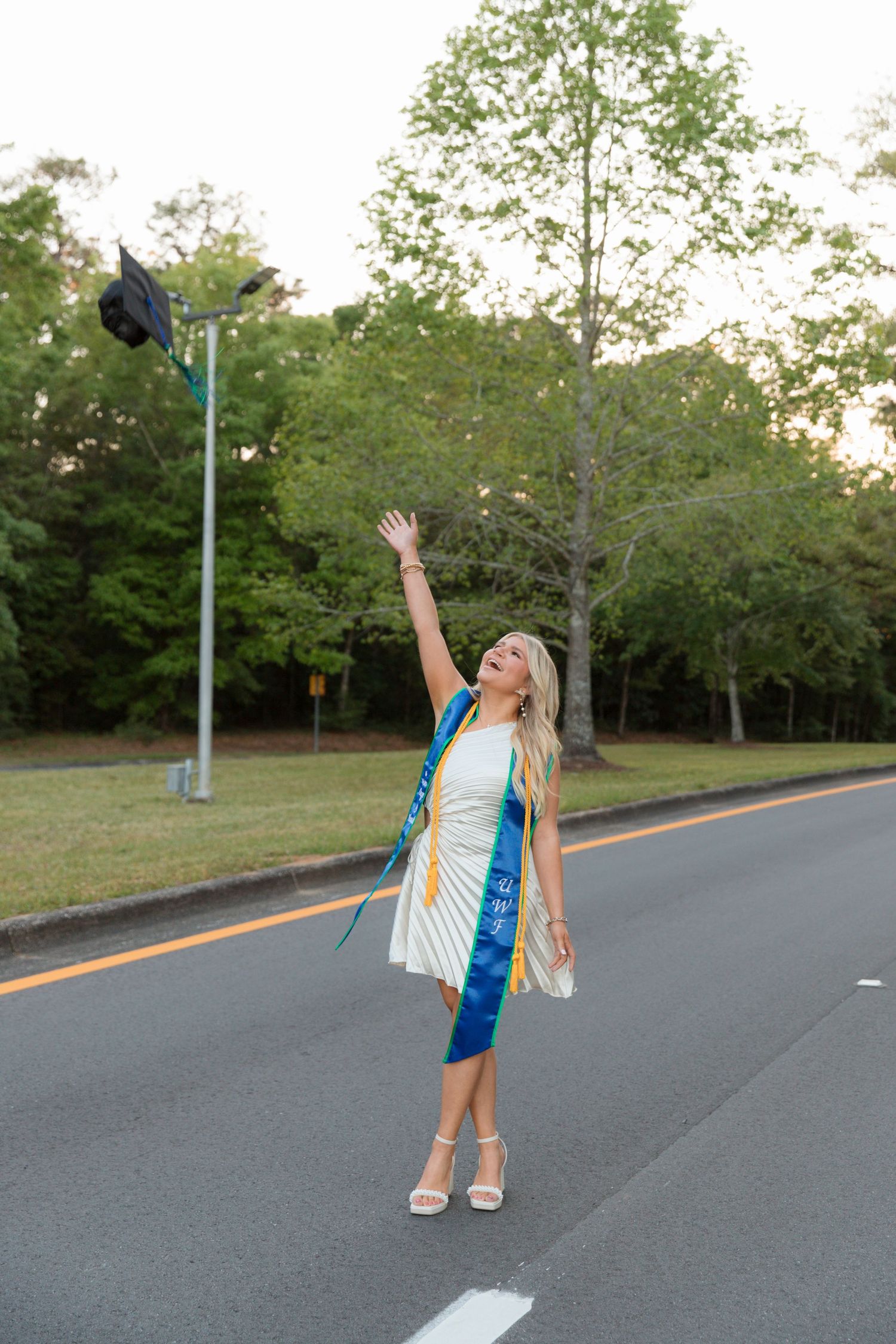 Graduate celebrating with arms raised on empty street during sunset photo shoot.