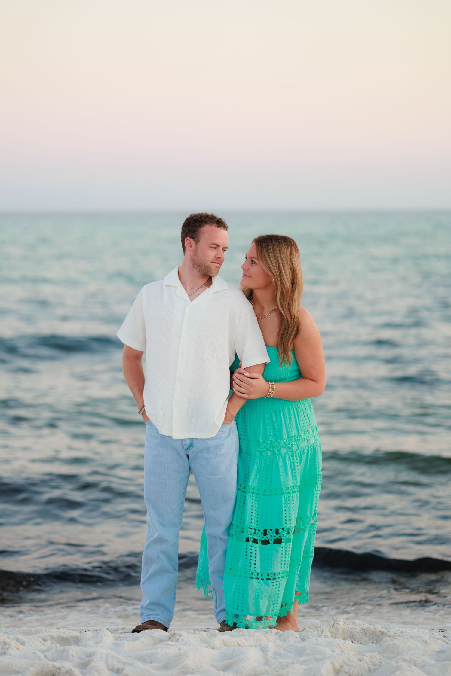 A romantic beach scene with a couple embracing by the ocean waves at dusk.