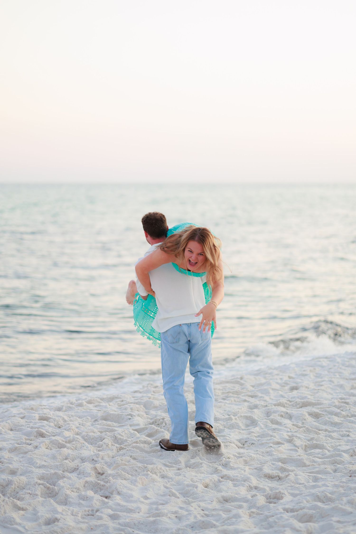 A playful piggyback ride on a white sandy beach at sunset with the ocean waves in the background.