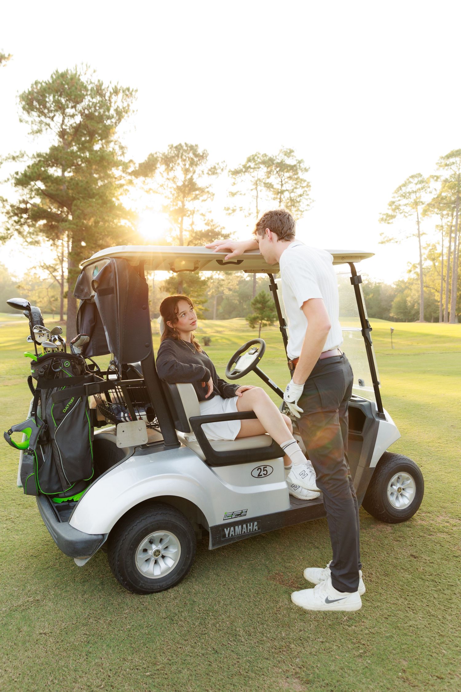 A couple poses with golf carts on a sunny golf course during sunset for romantic photos.