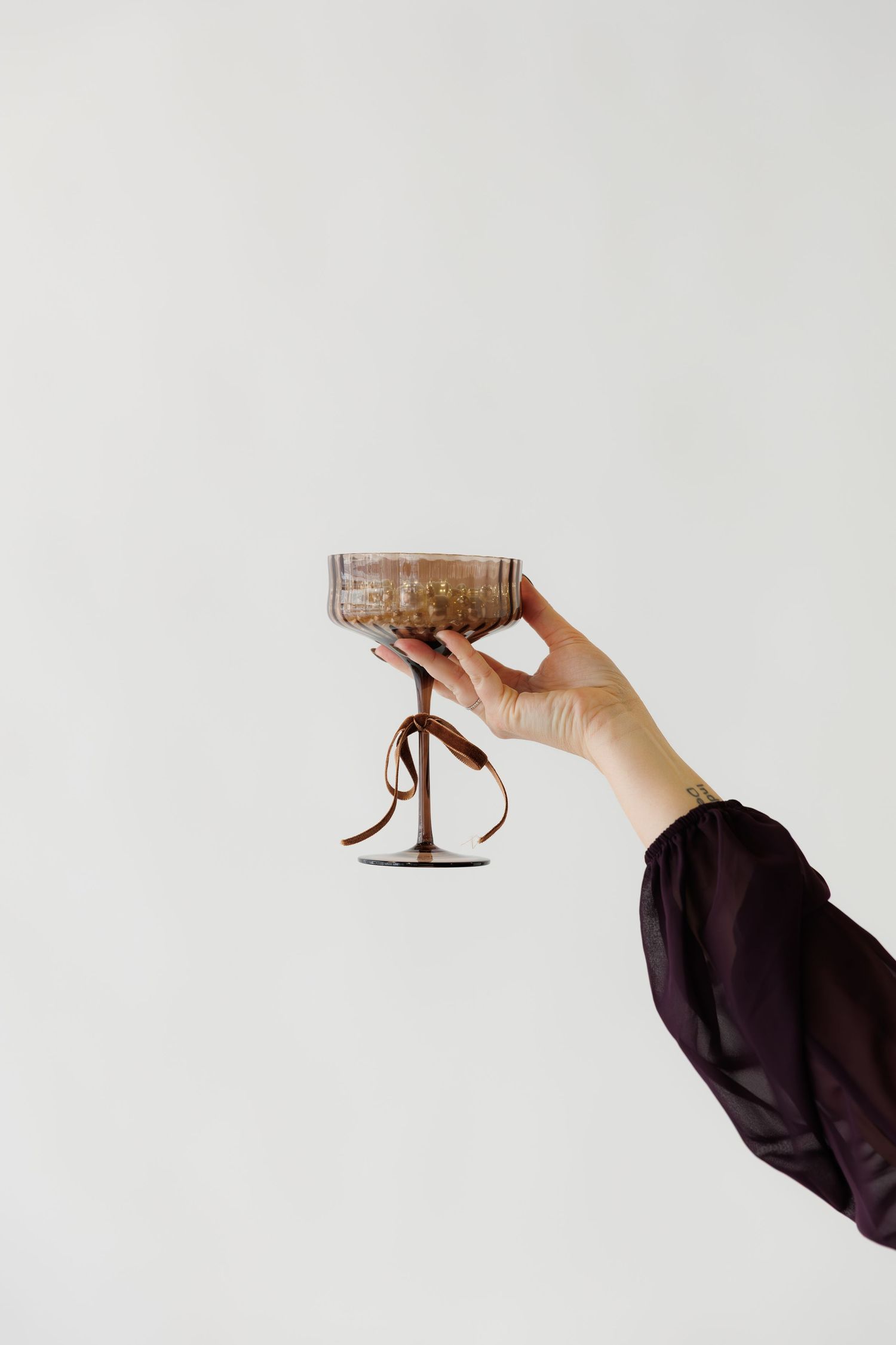 Hand holding up an ornate cocktail glass against white background.