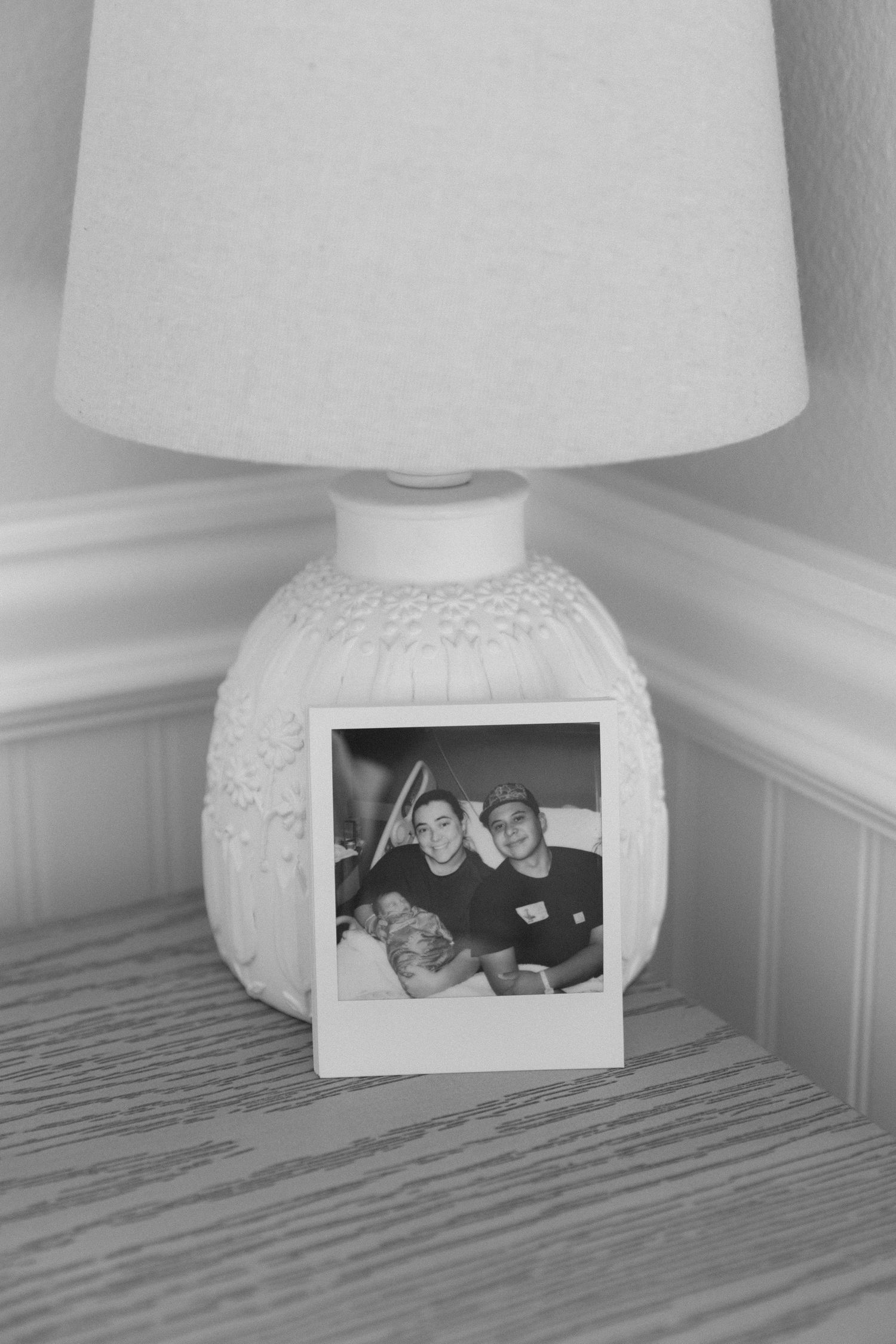 A series of four black and white photographs showing a white lamp base with a photo frame displayed beneath it.