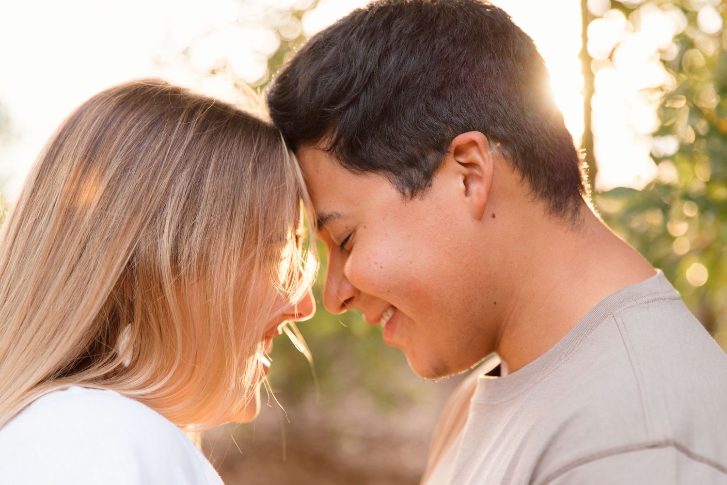 Young couple touching foreheads and smiling romantically outdoors in golden sunlight.
