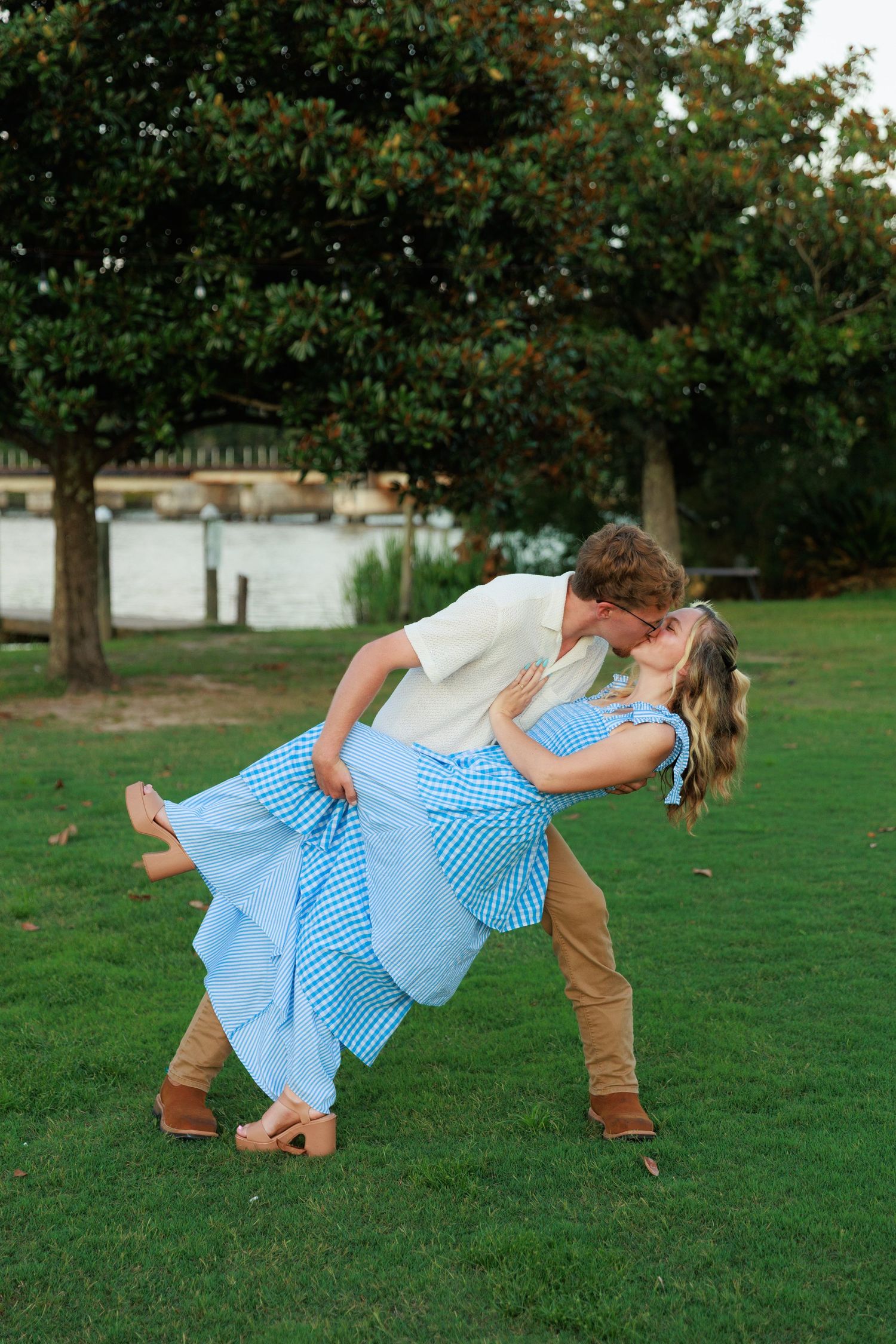 Couple sharing romantic dip kiss on green lawn near magnolia tree outdoors.