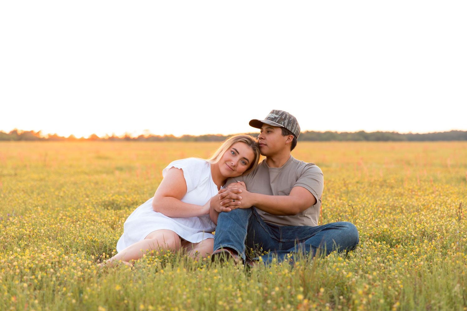 A couple sits together in a field of yellow wildflowers during golden hour.