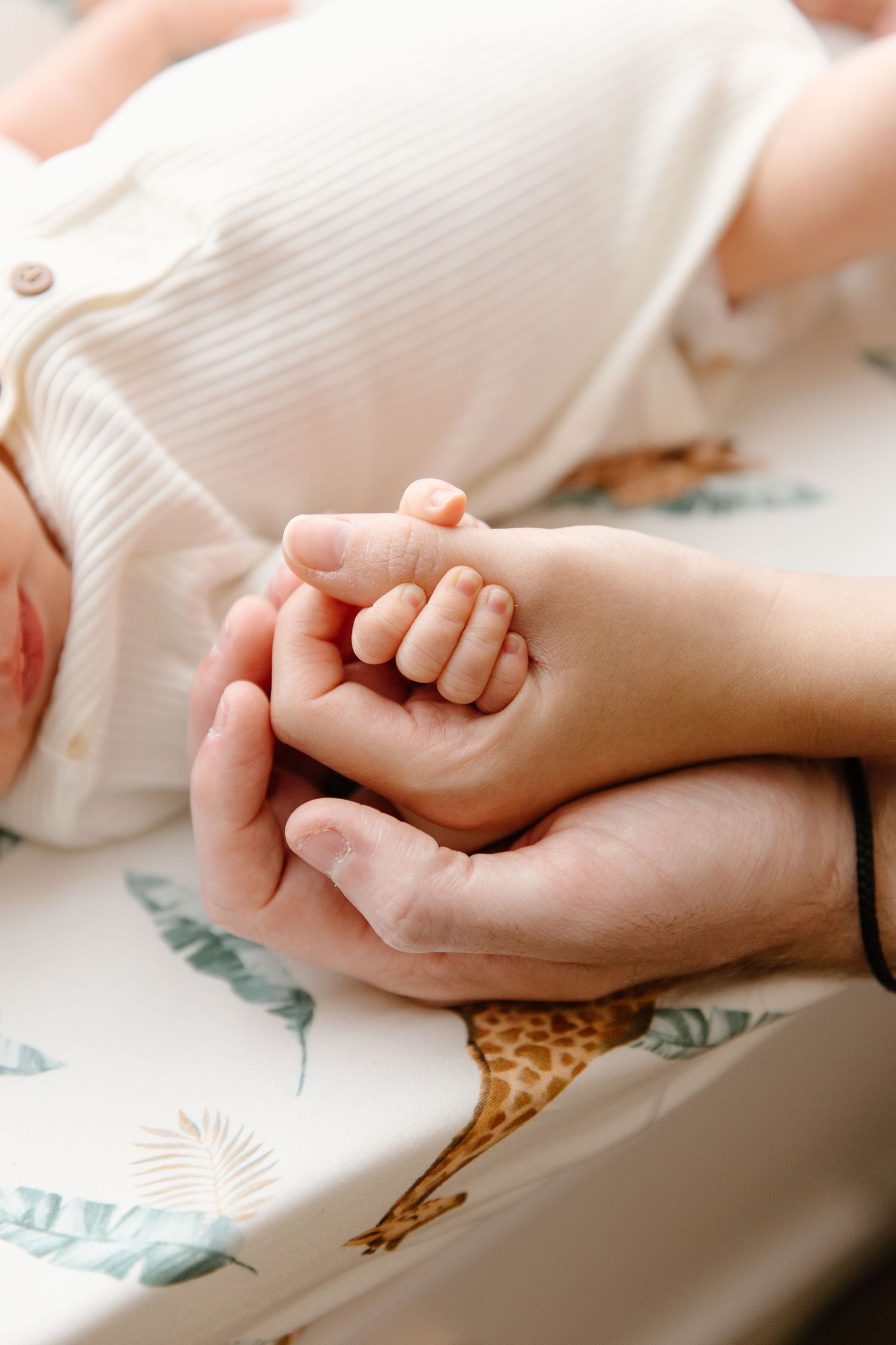 A close-up view of two hands tenderly clasped together against a soft white fabric background with floral pattern.