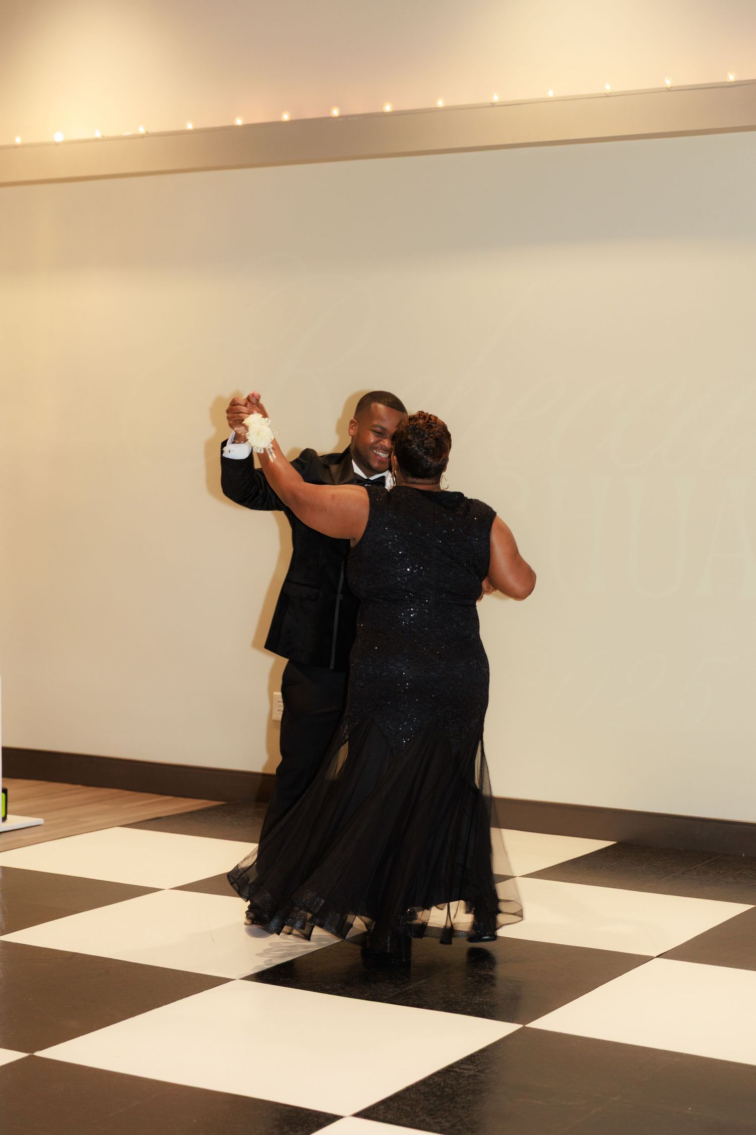 Wedding couple performs a playful dance move on a checkered dance floor.