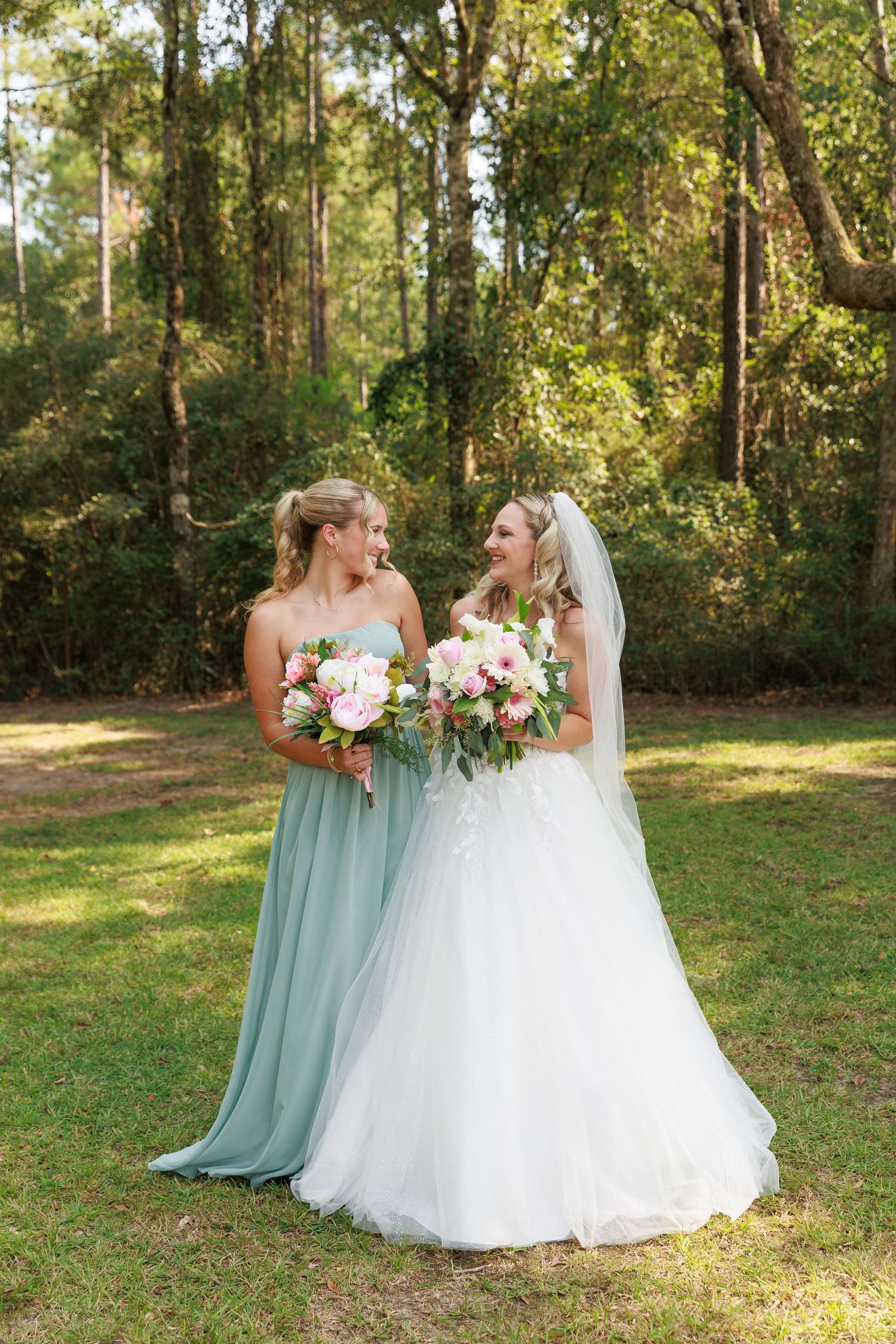 Wedding party members in mint green and white dresses share a candid moment in a sunlit outdoor garden setting.